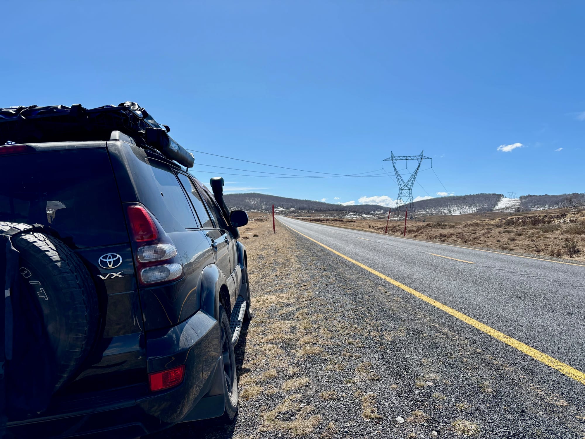 Our Prado with a rooftop tent, pulled over beside an empty highway across open high country, with patches of snow on the hills