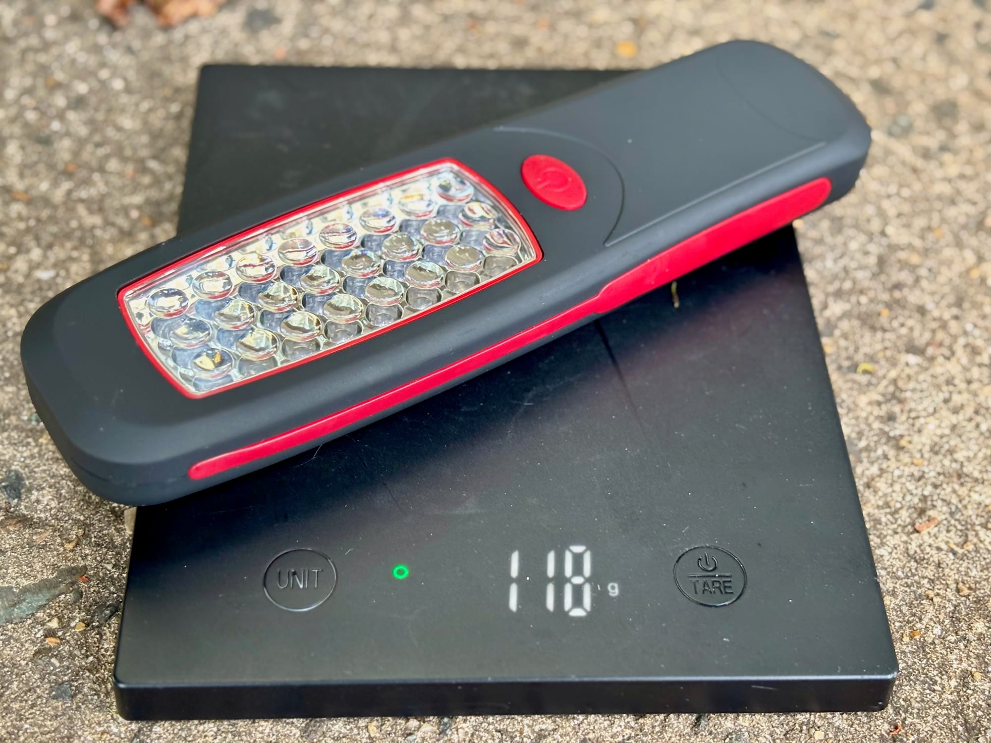 The Adventure Kings Illuminator LED work light without batteries on a scale showing 118 g
