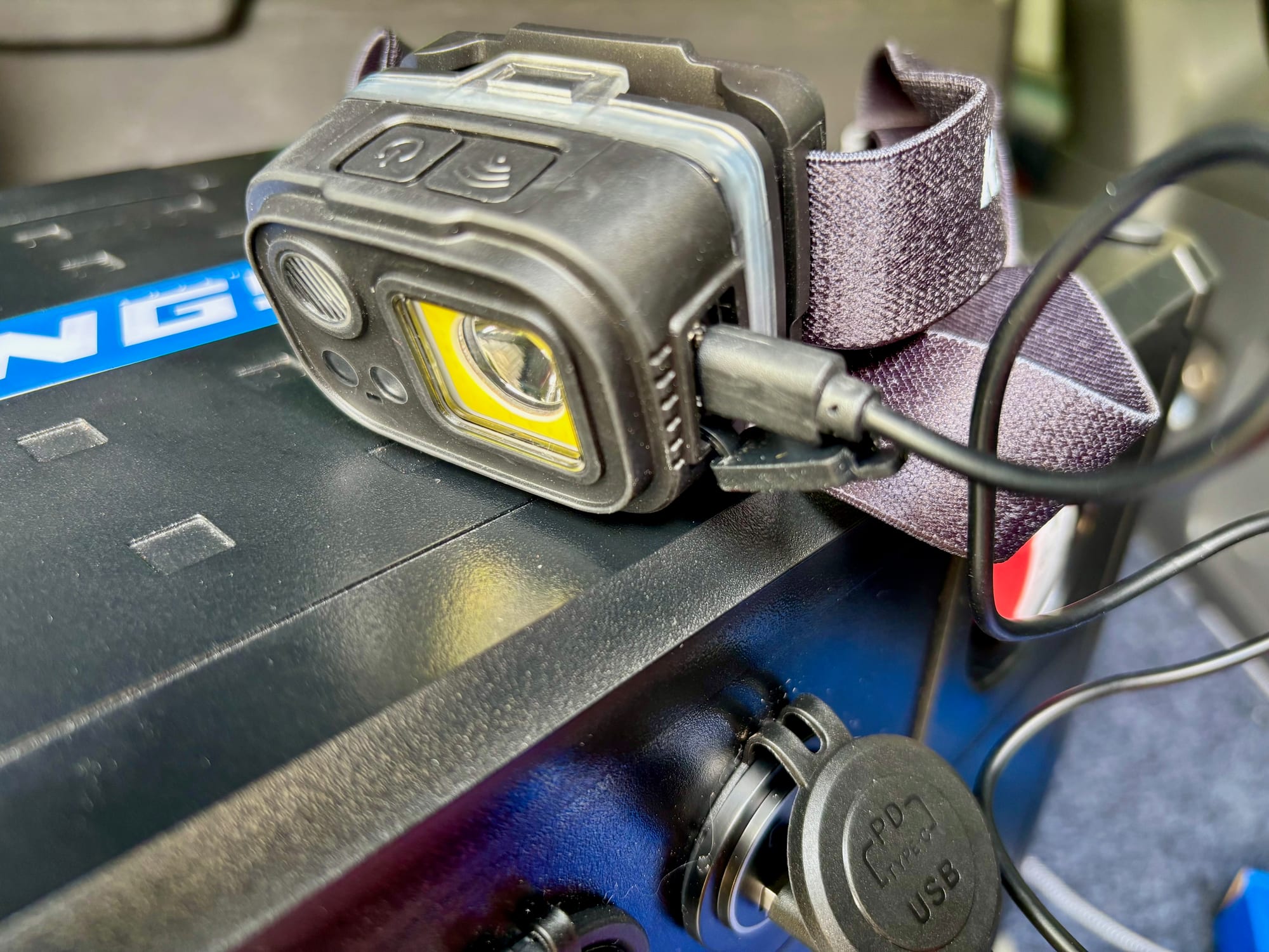 The Adventure Kings head torch charging over a USB-C cable on a battery box