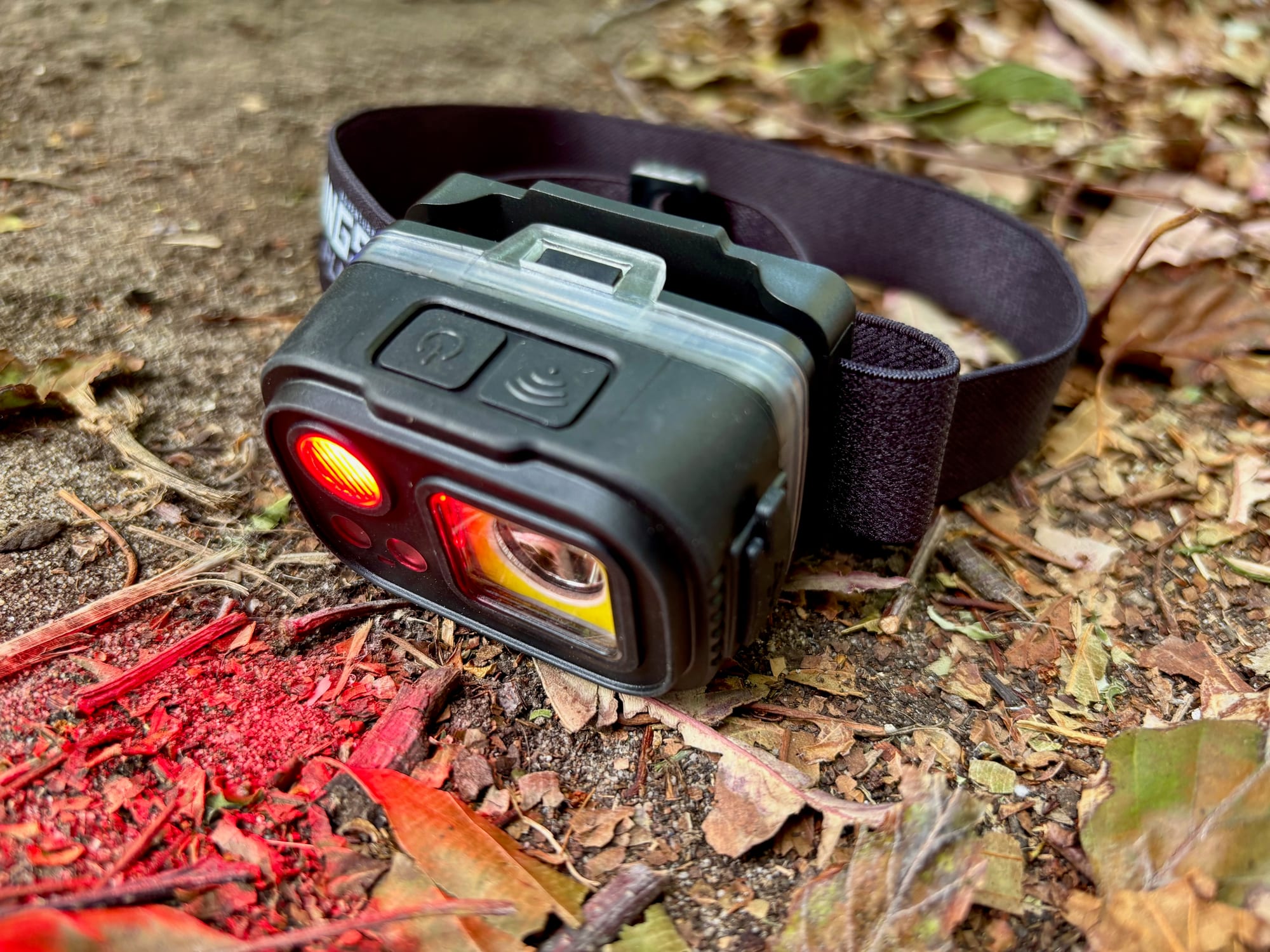 The Adventure Kings head torch with its red light on, lying on dry leaves