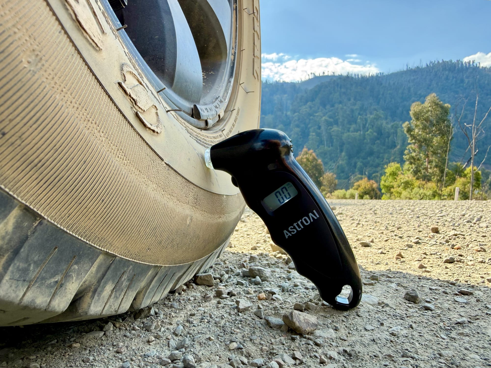 The AstroAI gauge leaning against a tyre on a gravel road in the hills