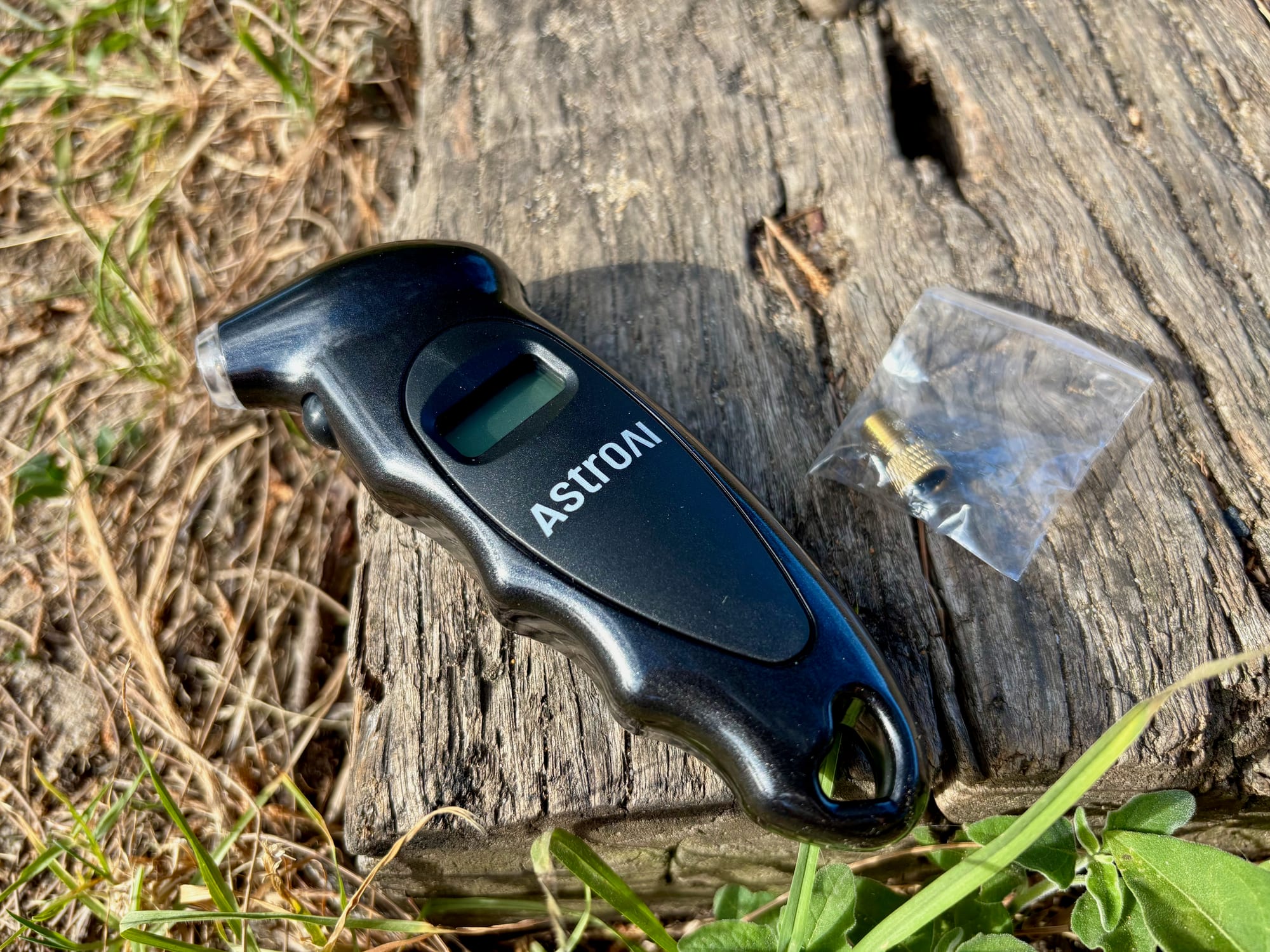The AstroAI digital tyre pressure gauge on a log, with its small brass valve adapter