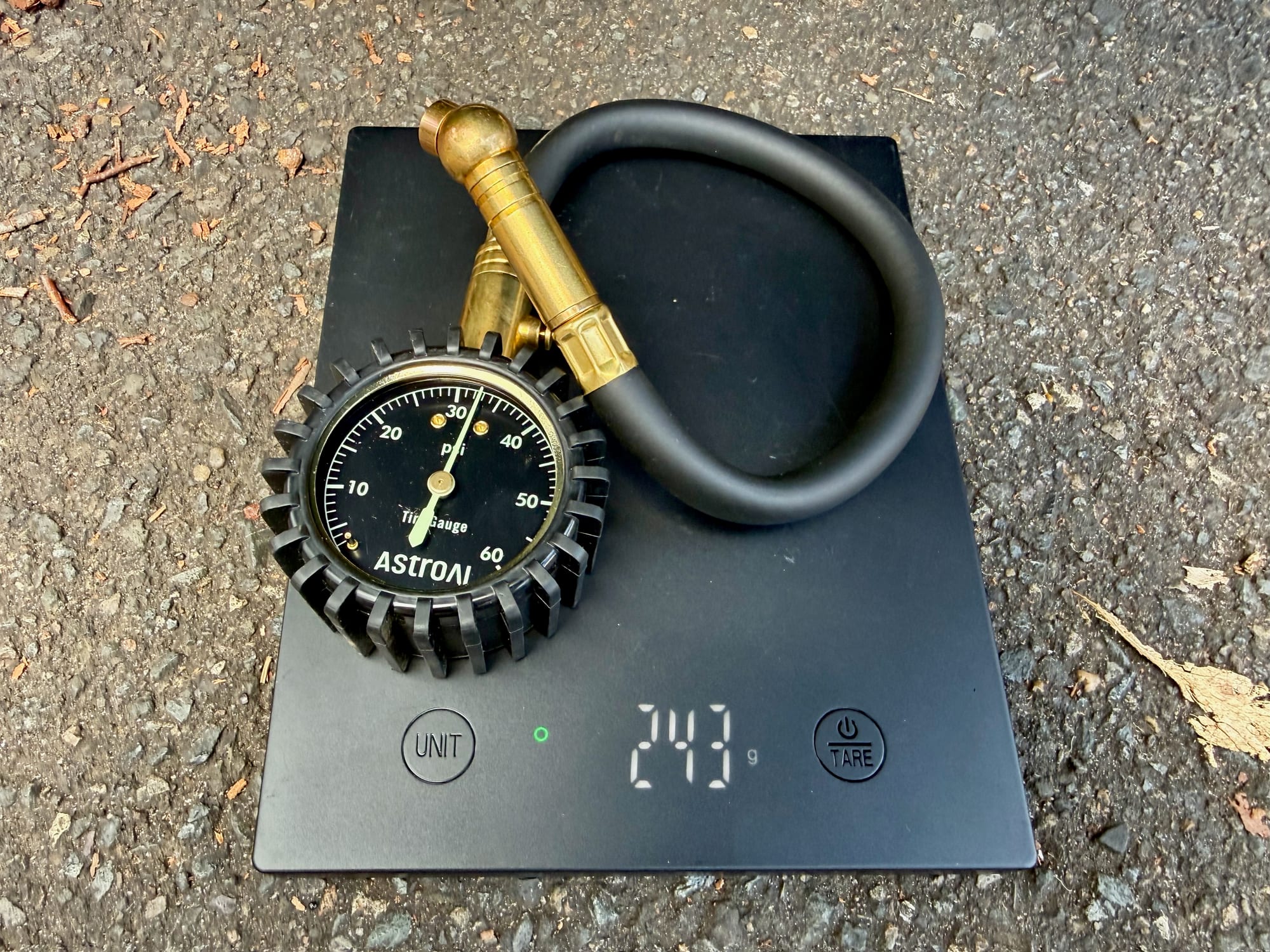 The AstroAI mechanical tyre pressure gauge on a scale showing 243 g