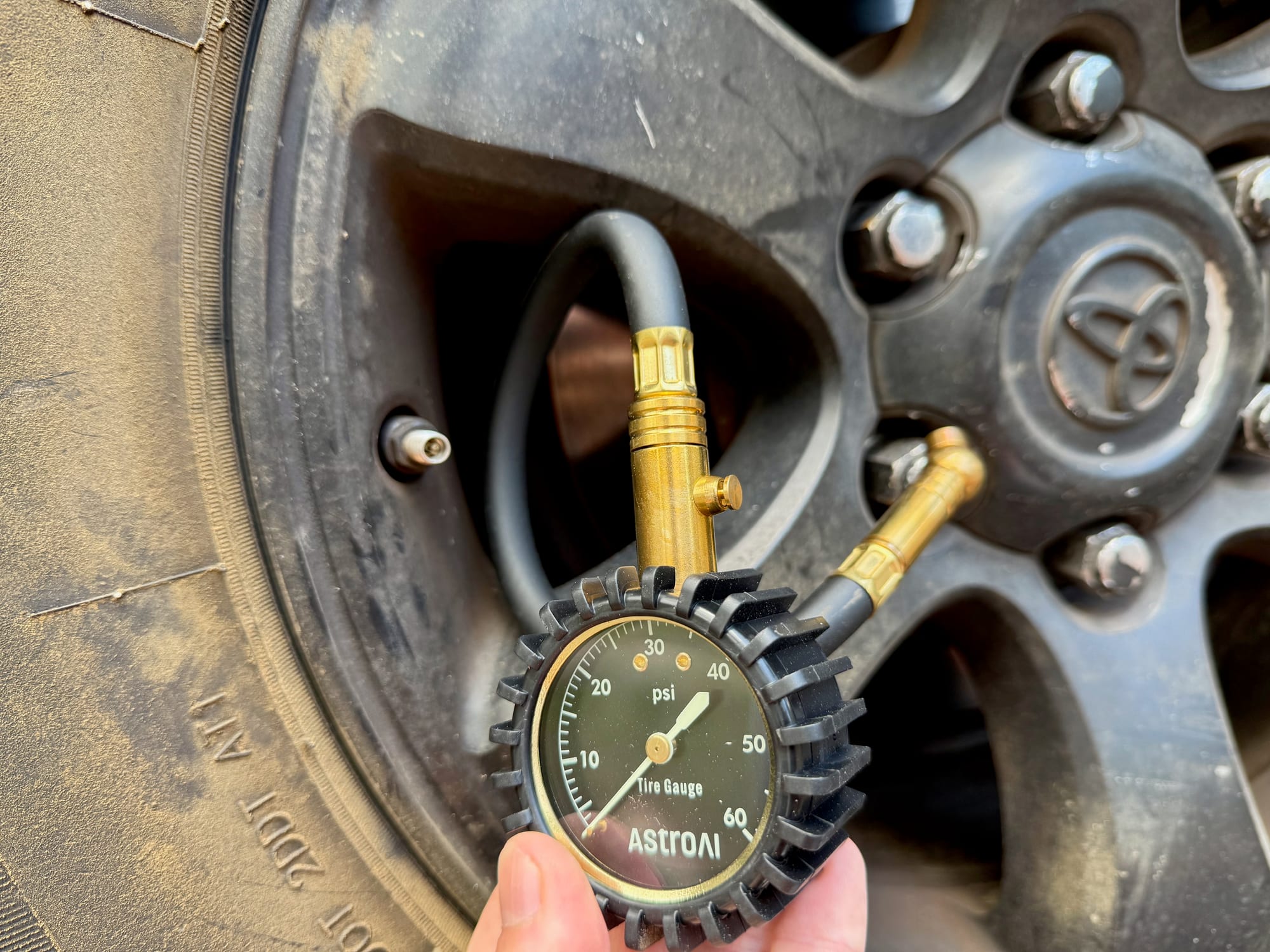The AstroAI mechanical tyre gauge held in front of a 4WD wheel, reading about 35 PSI