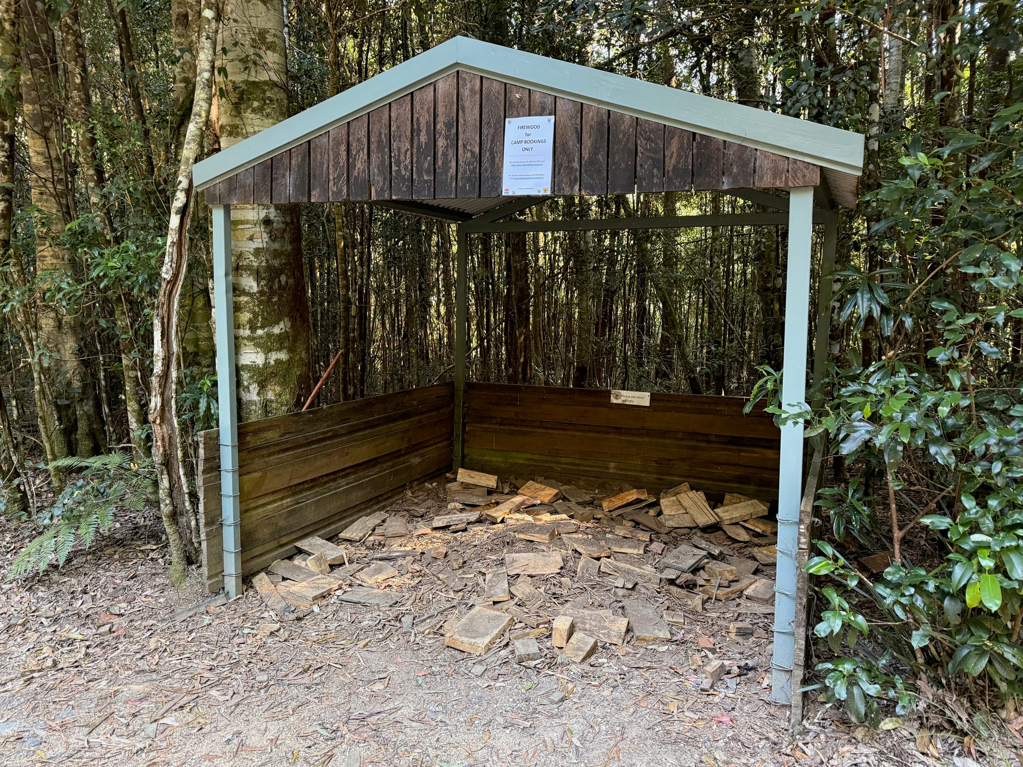 Split firewood on the ground inside the open timber woodshed at Bellbird Campground