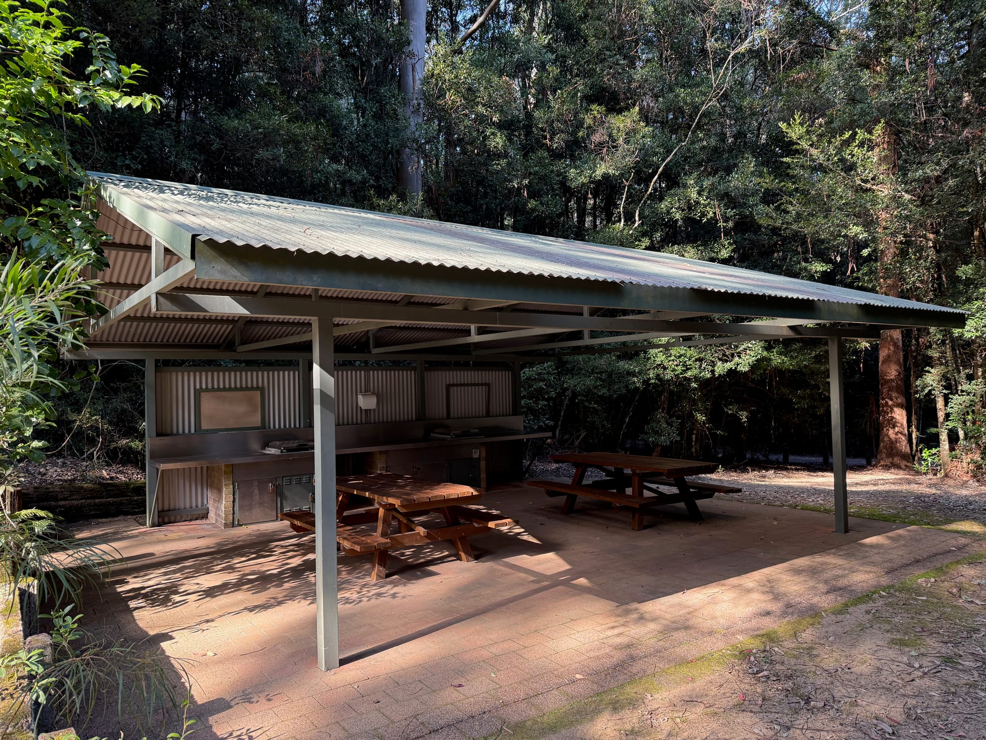 The roofed picnic shelter at Bellbird Campground with picnic tables and a bench along the back