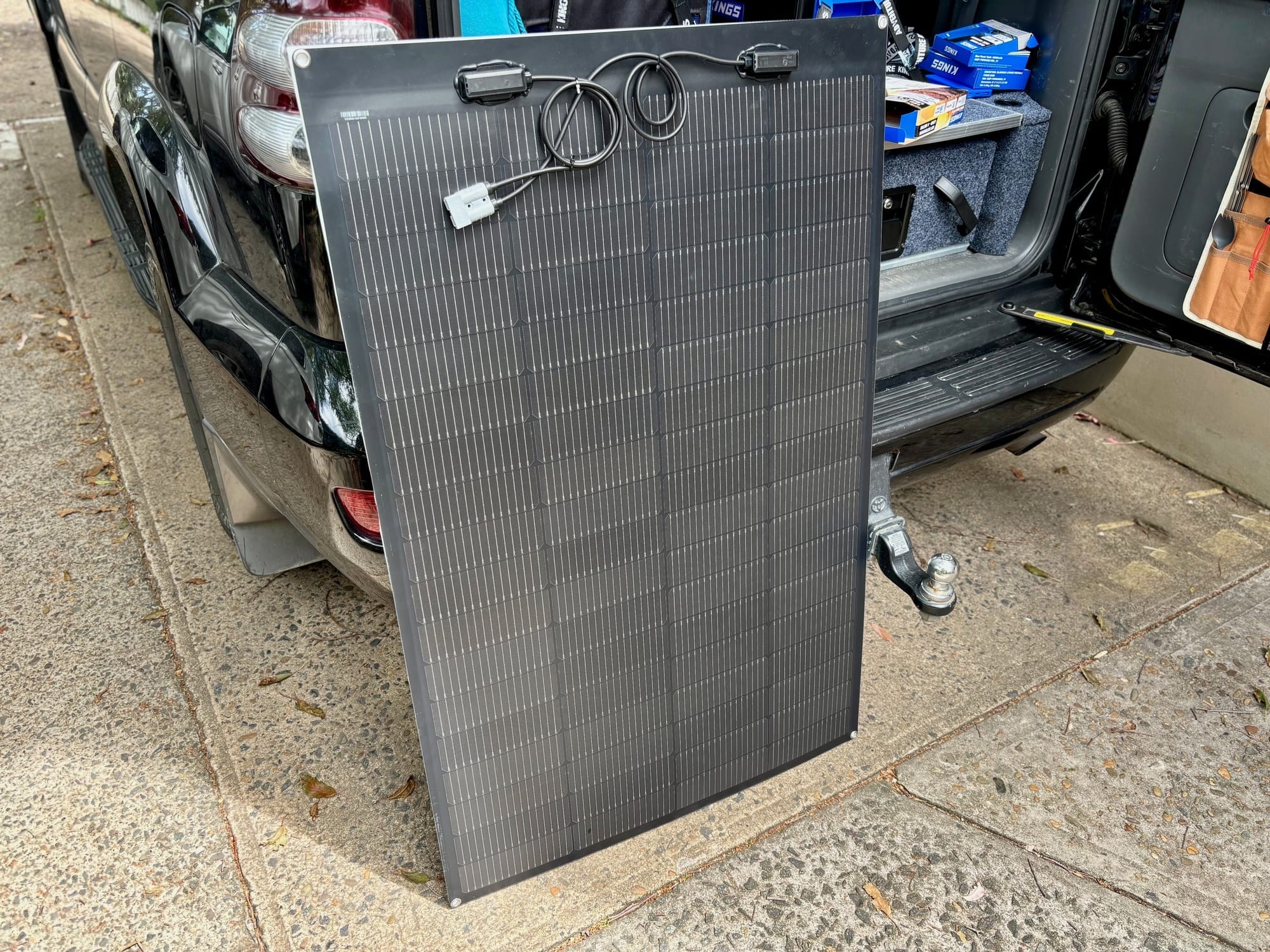 A semi-flexible solar panel with an Anderson plug leaning against the back of a 4WD, the rear door open