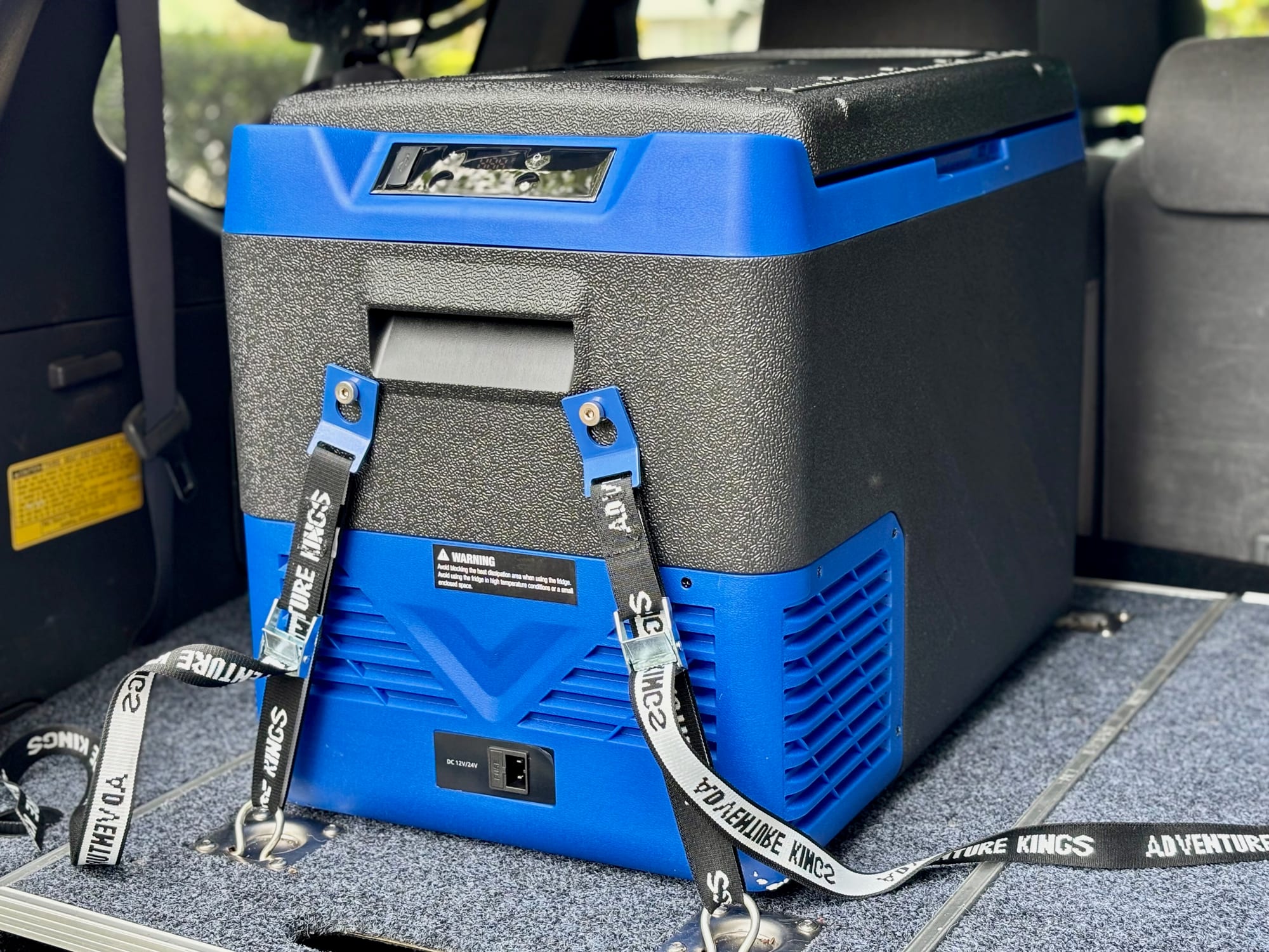 A blue and grey Kings Escape 40 fridge strapped down with tie-down straps in the back of a Prado