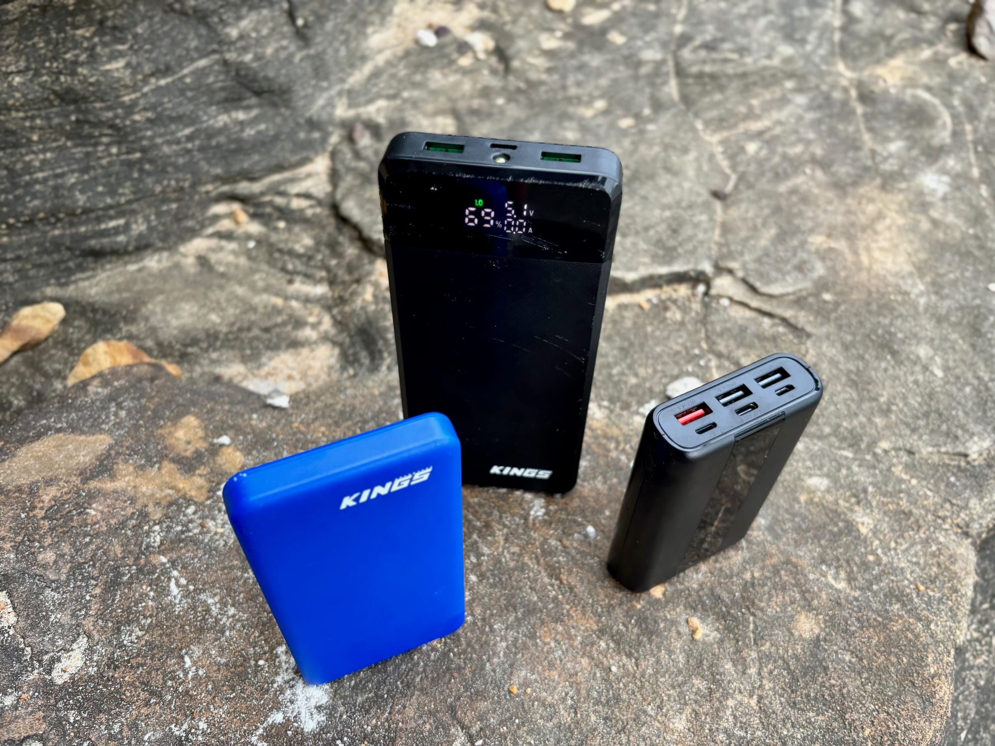 A blue Kings 10,000mAh, a Kings 20,000mAh and a VRURC 20,000mAh power bank on a rock
