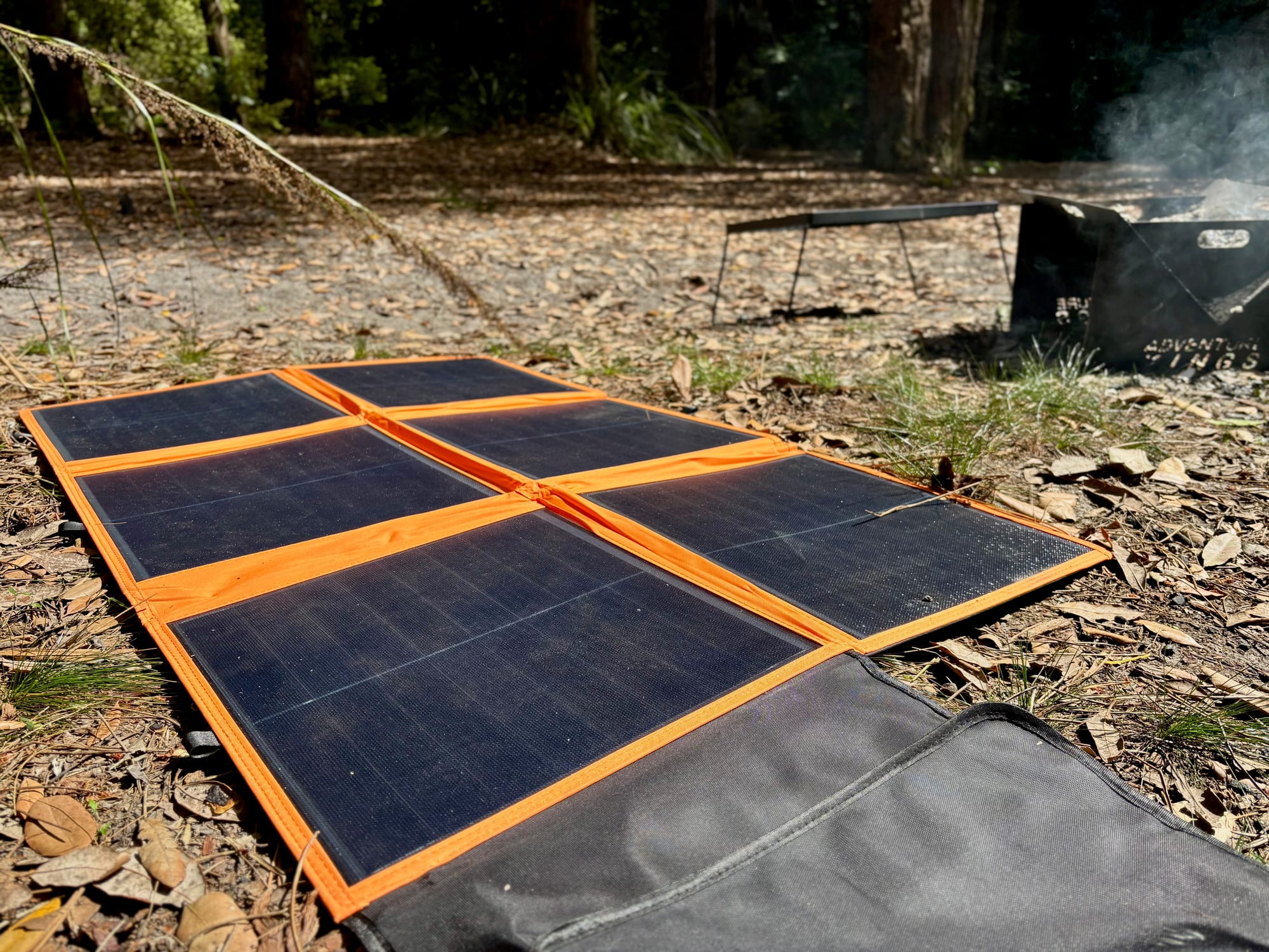 A folding solar blanket laid out on the ground in the sun at a bush campsite, its carry bag beside it