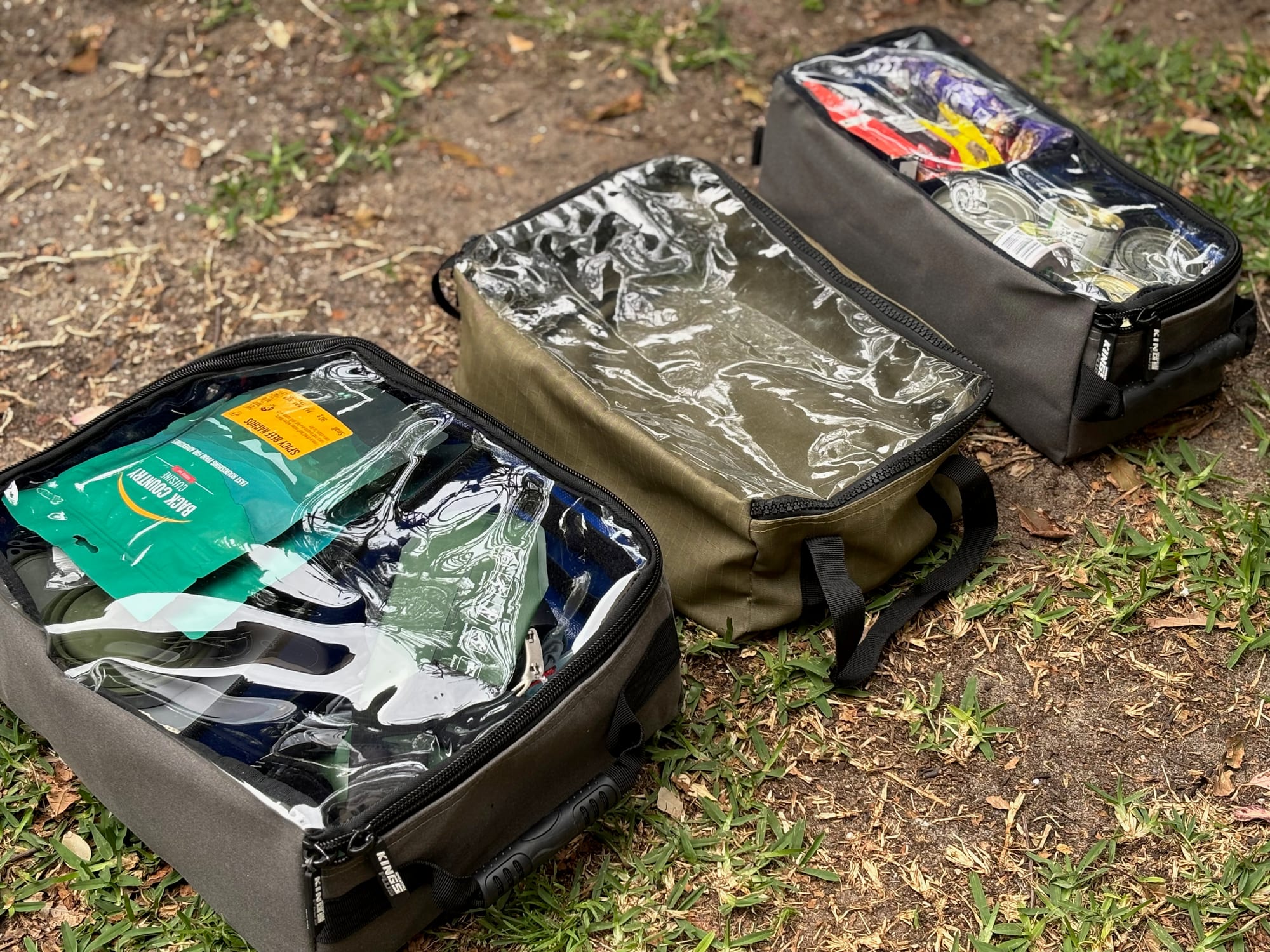 Three packed clear-top canvas storage bags lined up on the grass