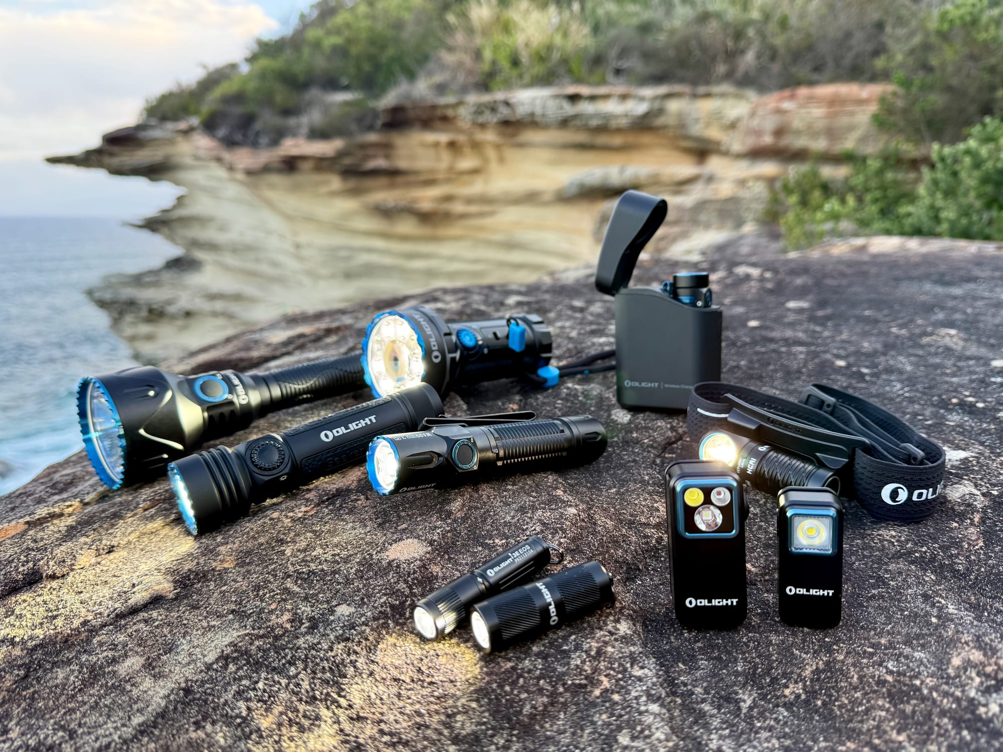 Our Olight torches, from keychain lights to a big spotlight, laid out on a sandstone rock above the sea at Bouddi National Park