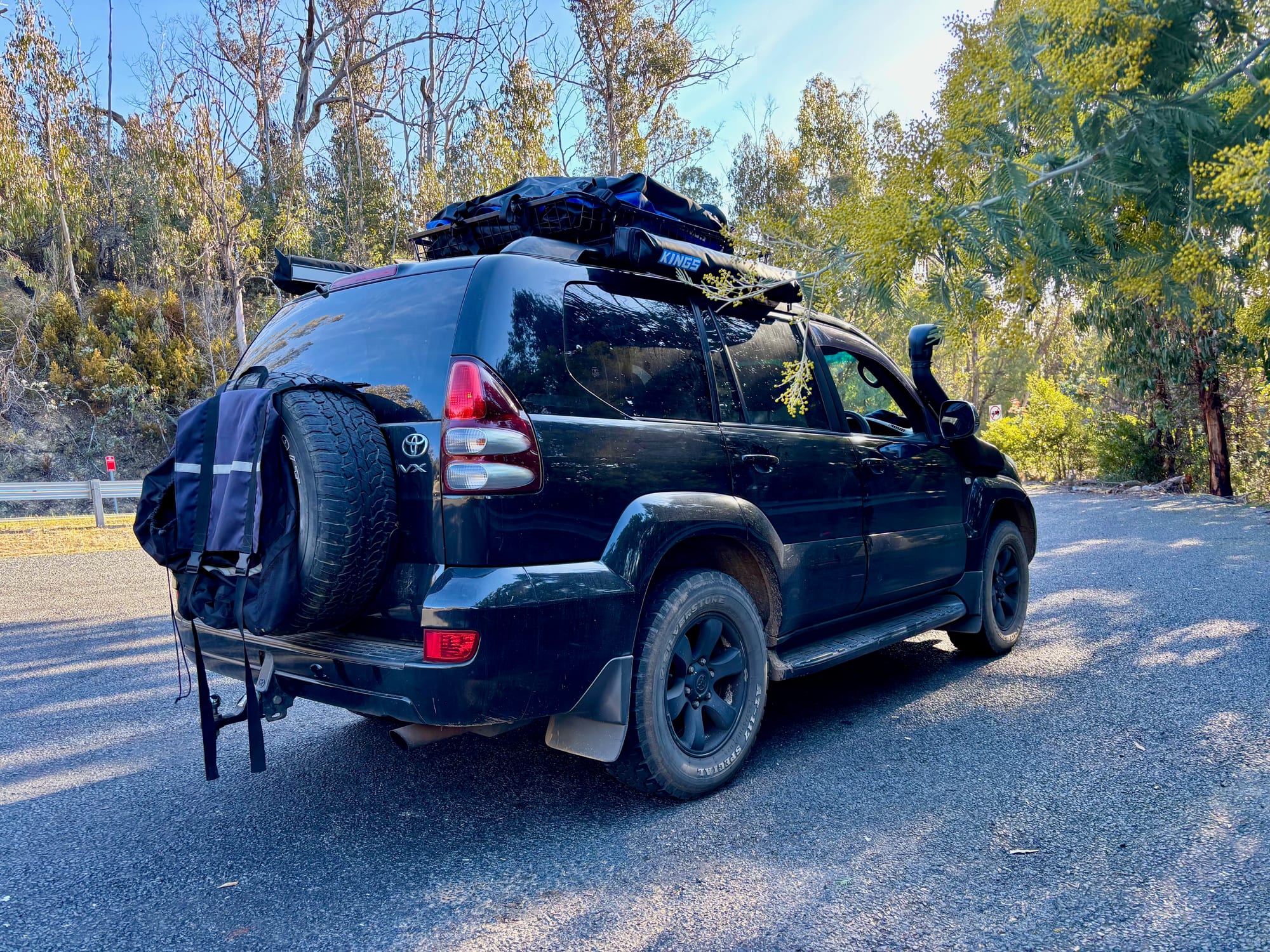 Our 4WD parked on the bitumen beside the highway at Black Perry Lookout, with wattle in flower behind