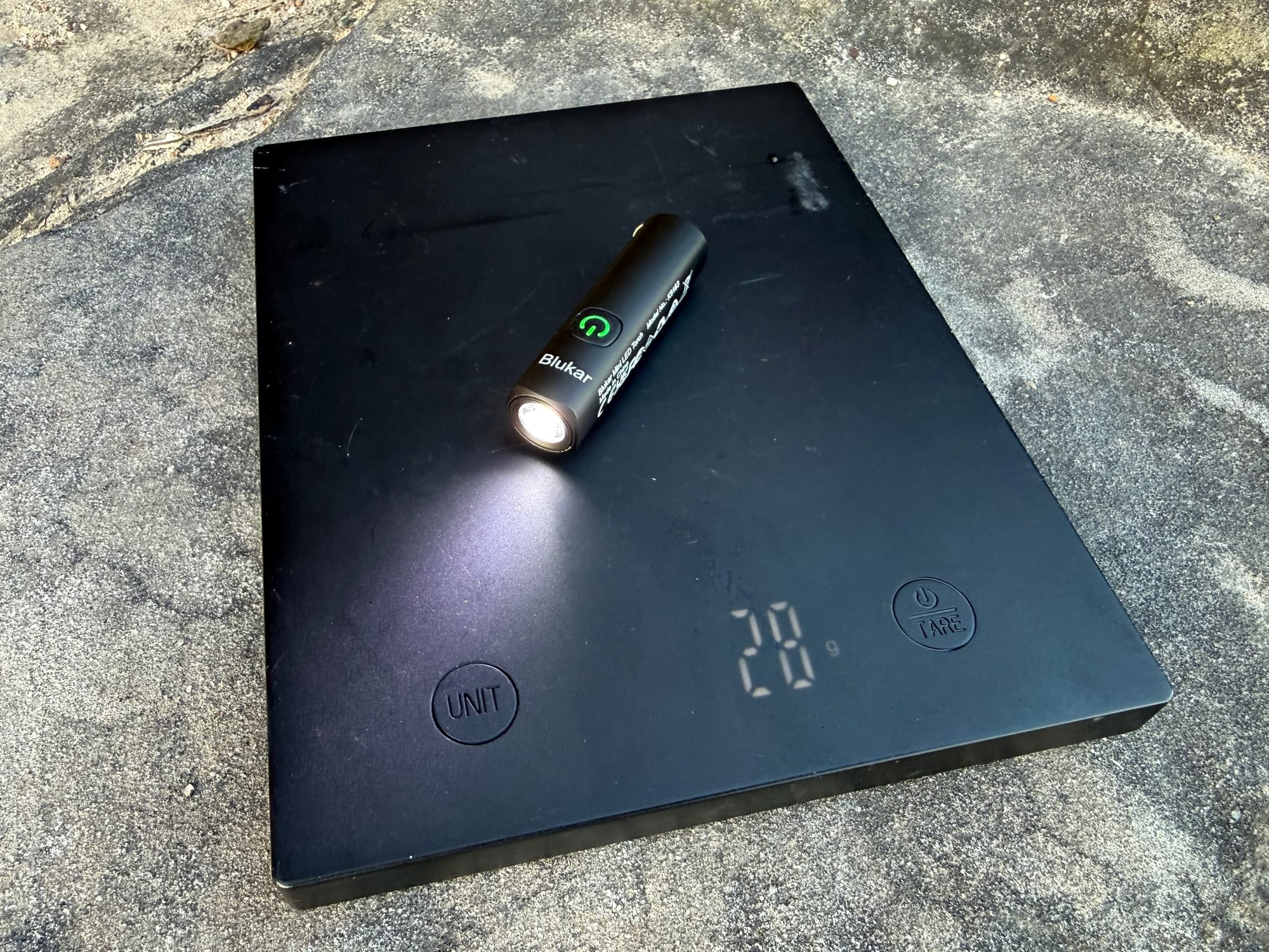 The Blukar Mini Torch switched on, on a digital scale showing 28 grams