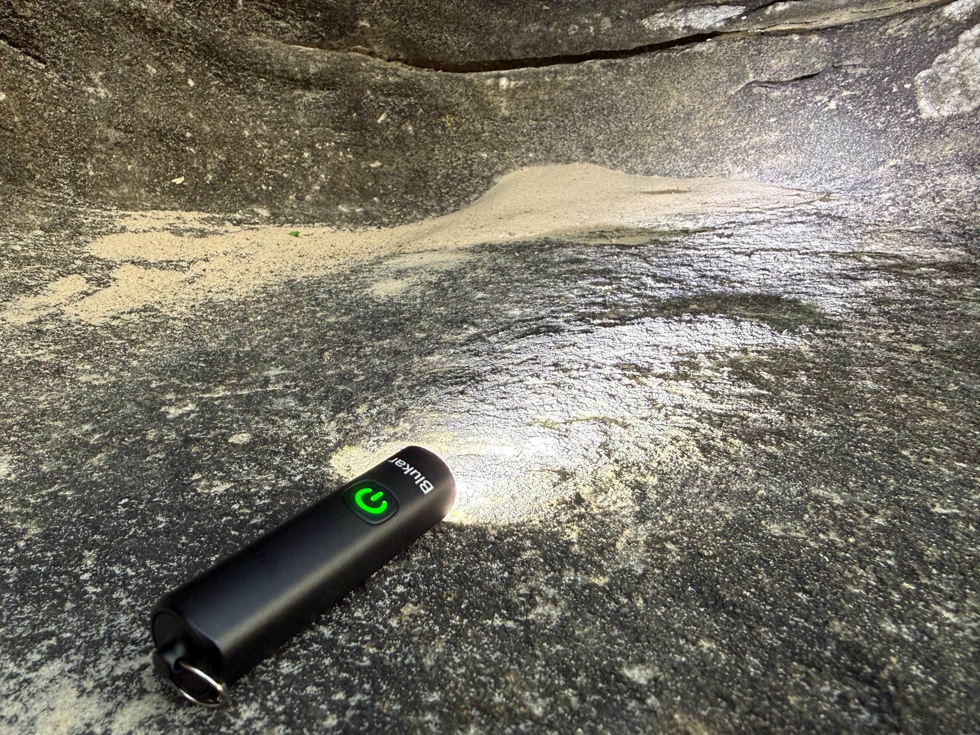The Blukar Mini Torch lying on a rock, lighting up the rock face in front of it