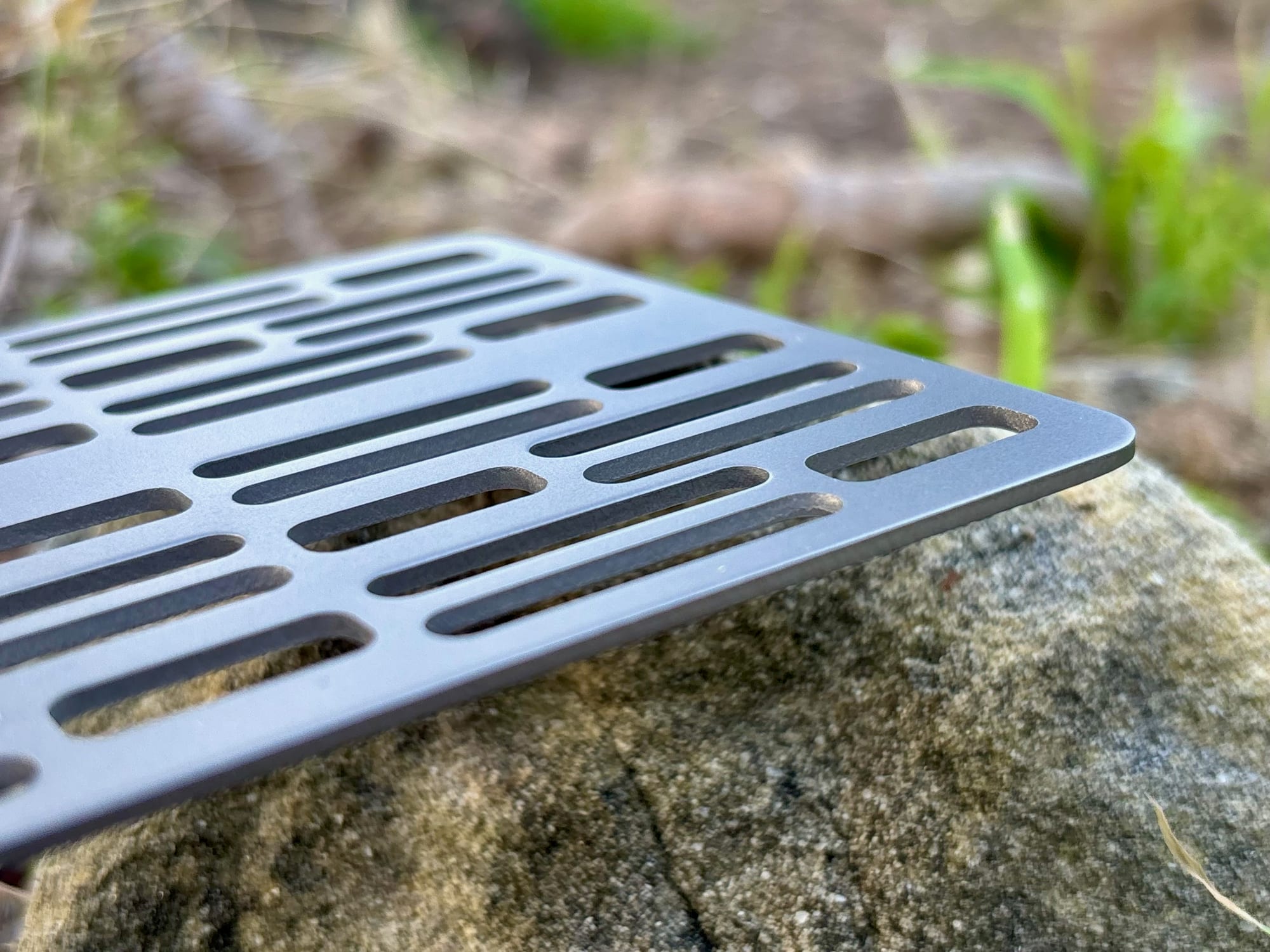 The edge of the Ti2023C titanium grill plate resting on a rock, showing its thickness