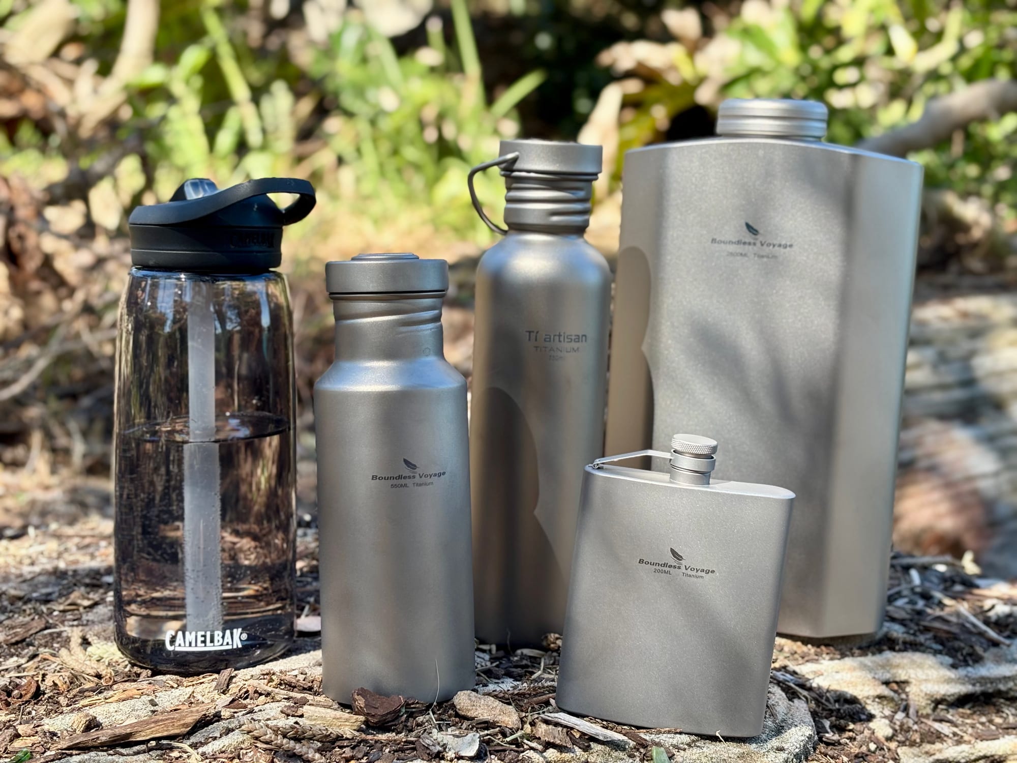 The 200 ml hip flask standing in front of three titanium water bottles and a plastic bottle in the bush