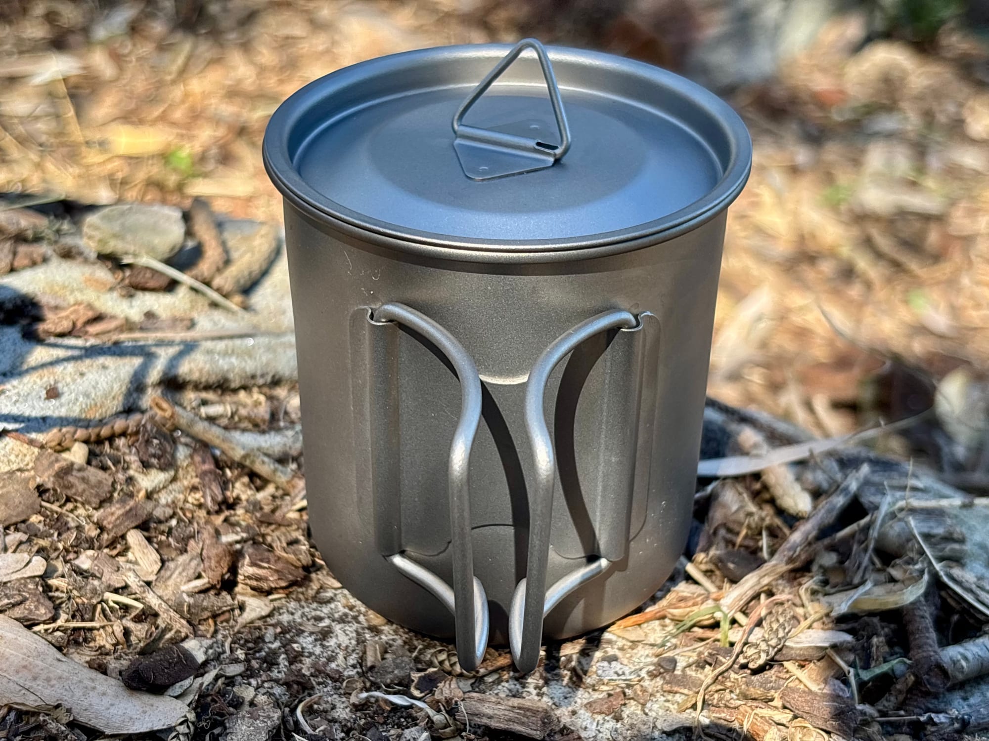 The titanium mug with its lid on and the two wire handles folded flat against the side