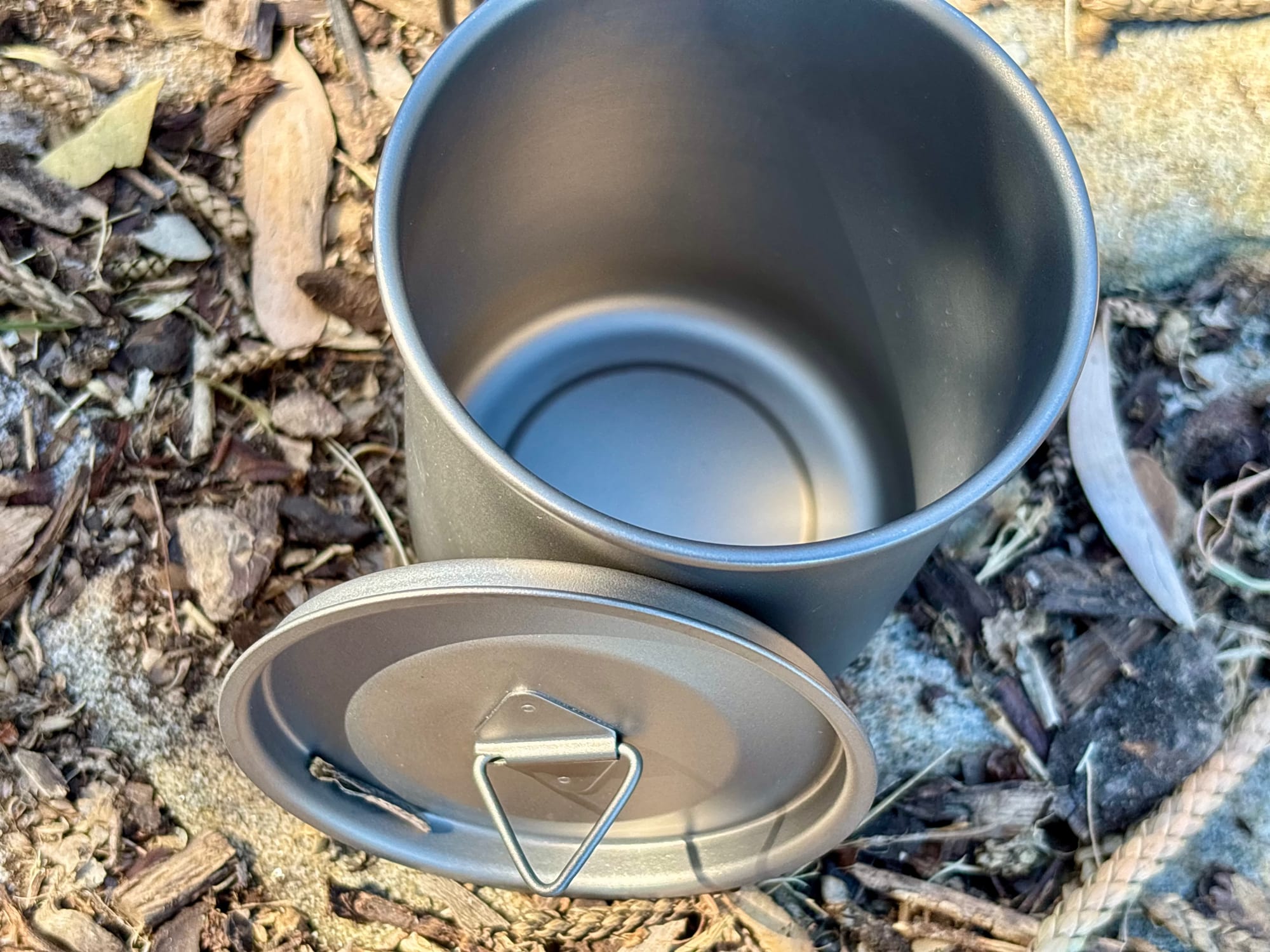 The open titanium mug with its lid beside it, showing the triangle lifting tab