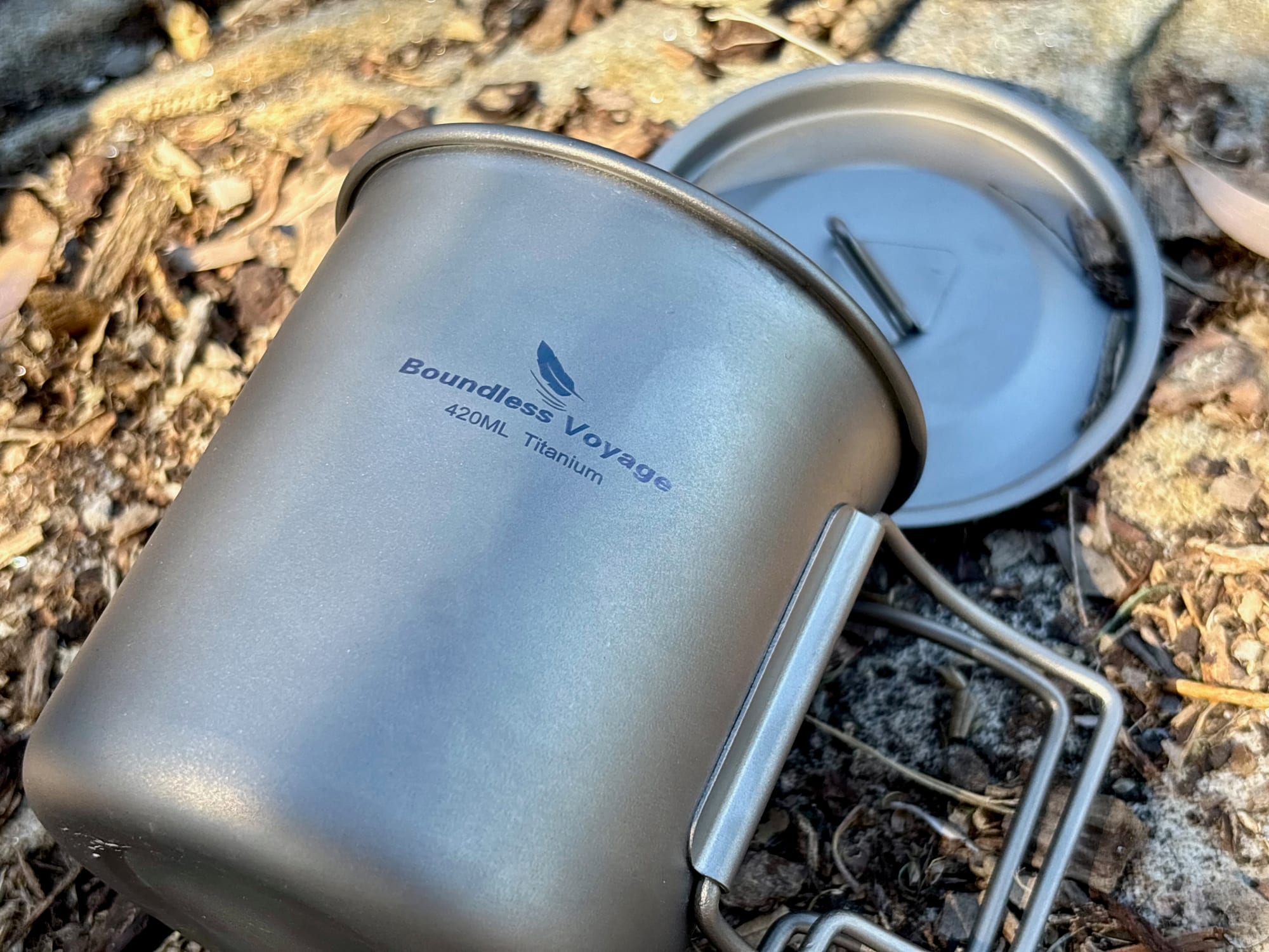 The 420 ml titanium mug lying on its side next to its lid, with the Boundless Voyage 420ML Titanium marking
