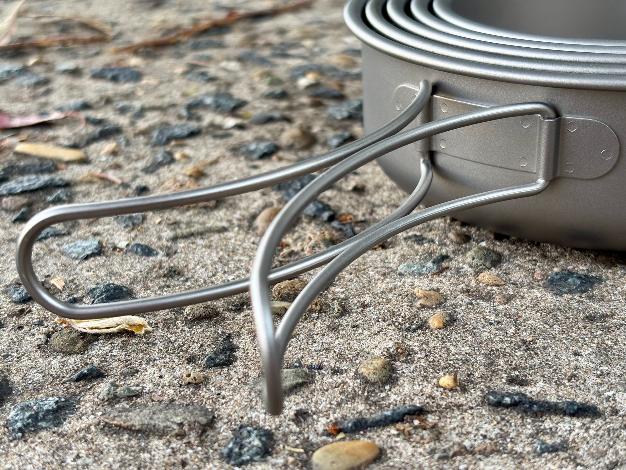 A folding wire handle swung out from the side of a Boundless Voyage titanium pan
