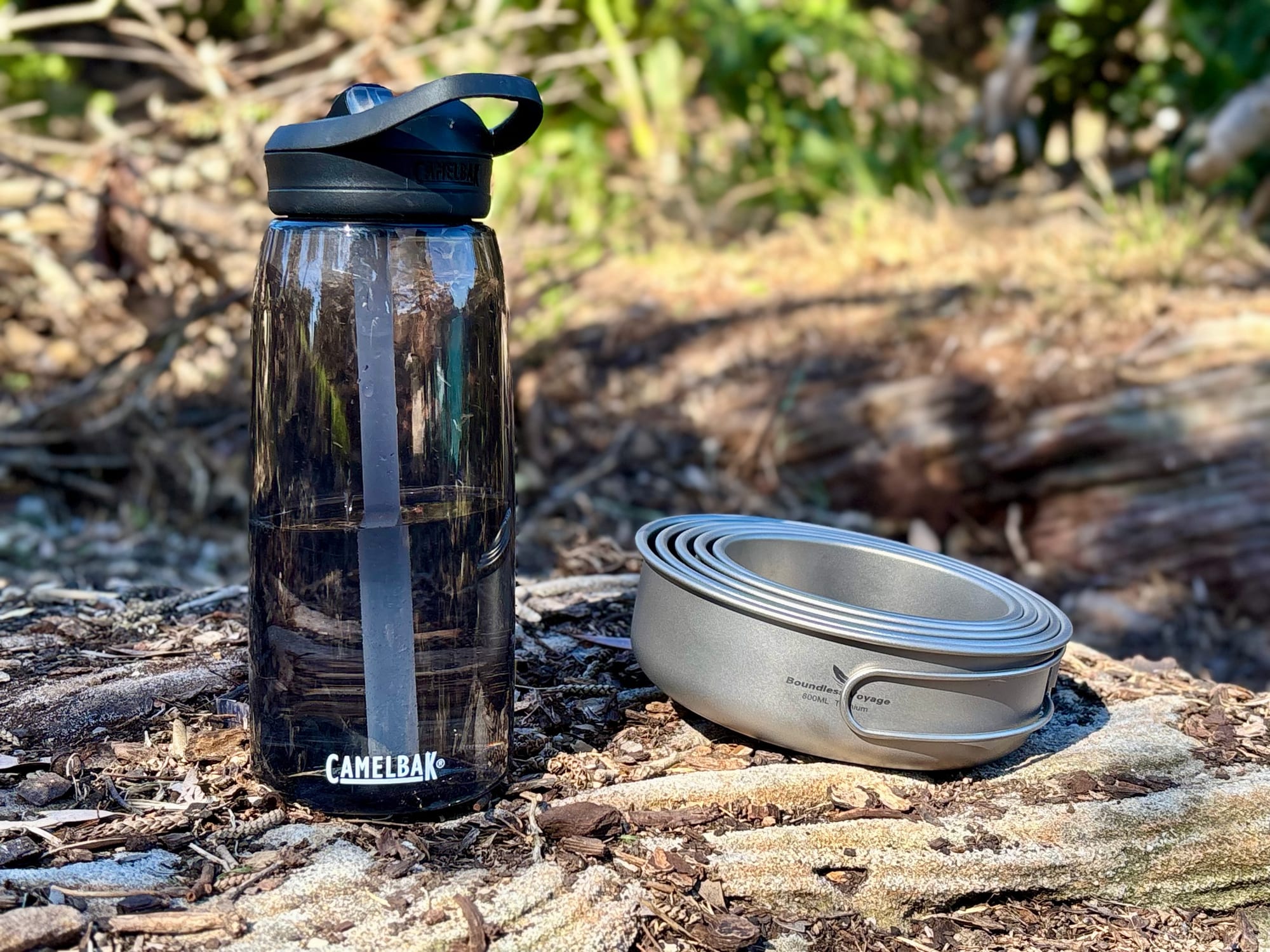 The nested Boundless Voyage pans next to a 1 litre CamelBak water bottle on a rock