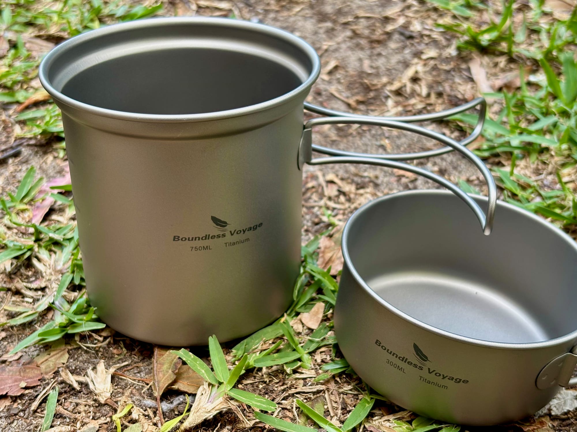 The Boundless Voyage 750 ml titanium pot and the 300 ml pan side by side on the grass