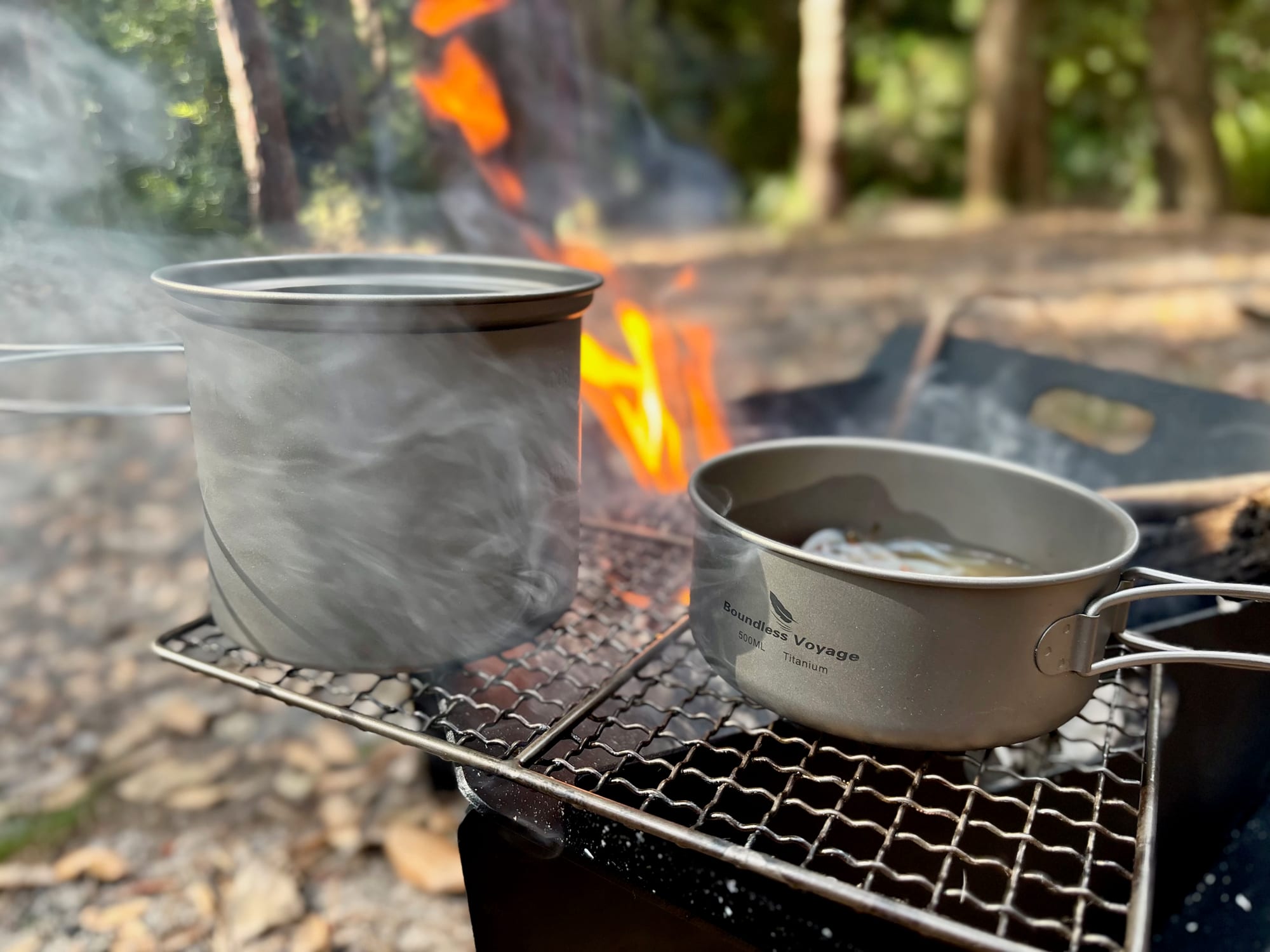 Water steaming in the titanium pot next to the pan on the grill
