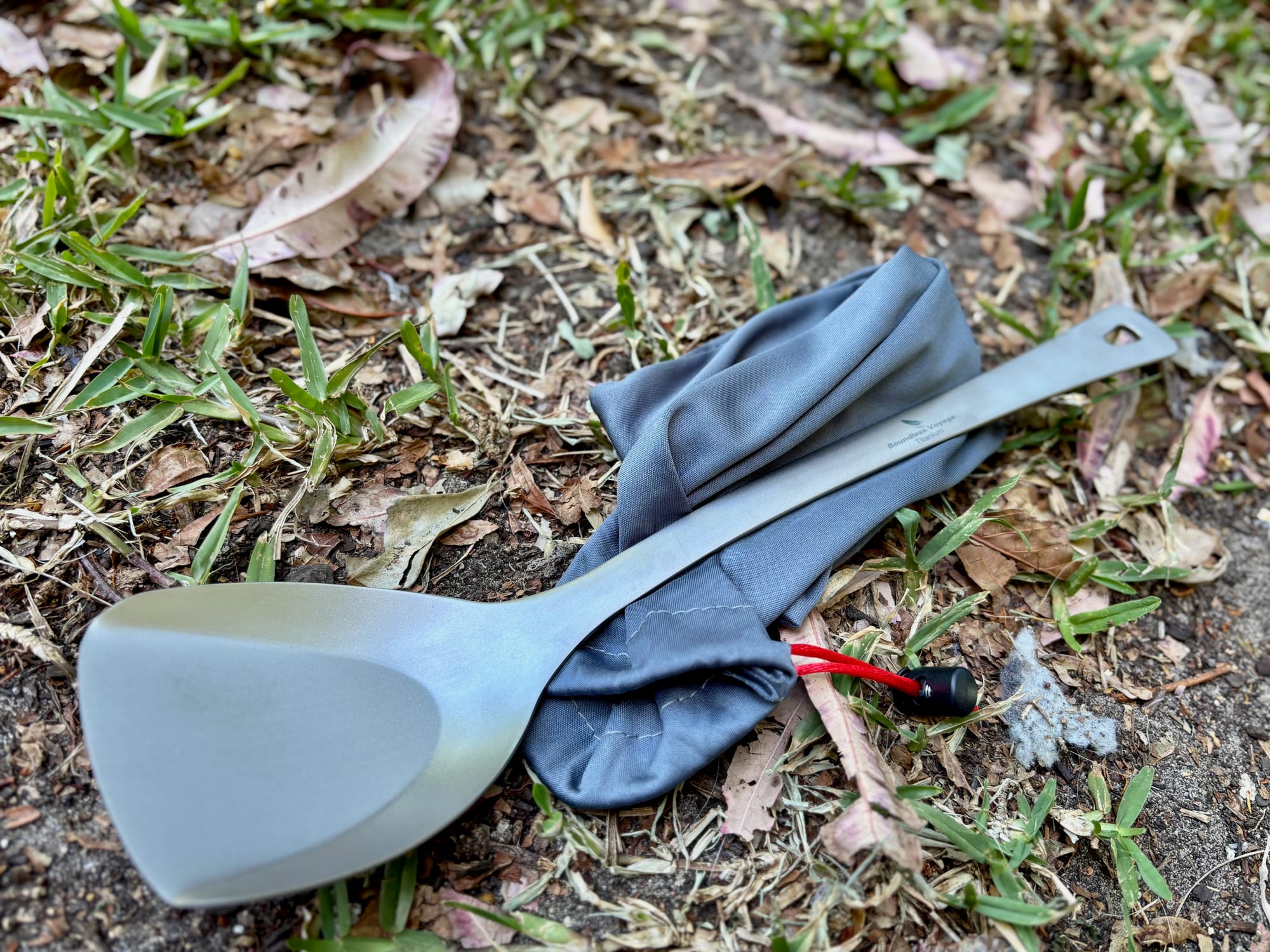 The Boundless Voyage Ti1073T titanium spatula on the grass with its grey drawstring bag