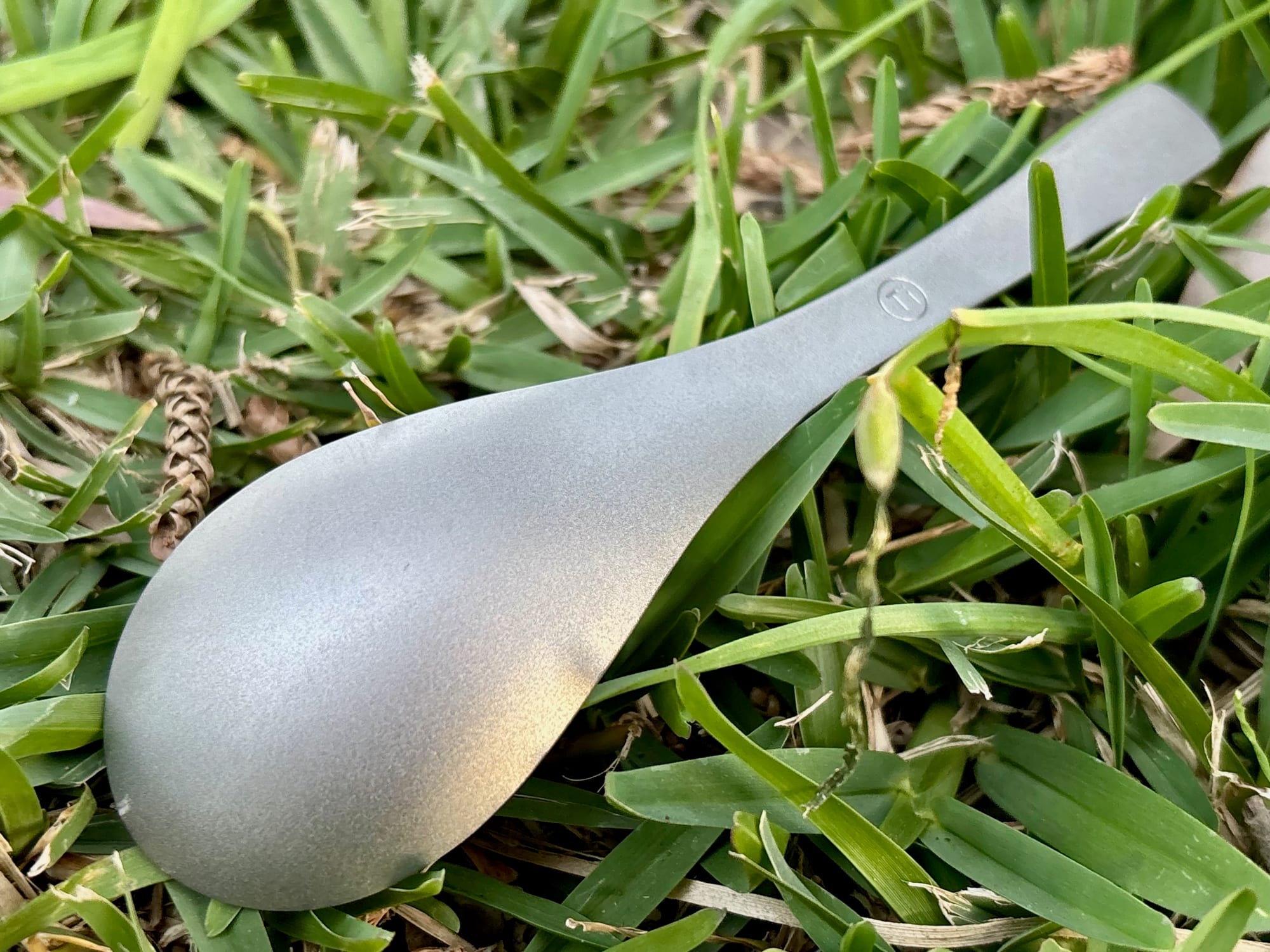 Close-up of the deep, rounded bowl of the titanium spoon lying in the grass