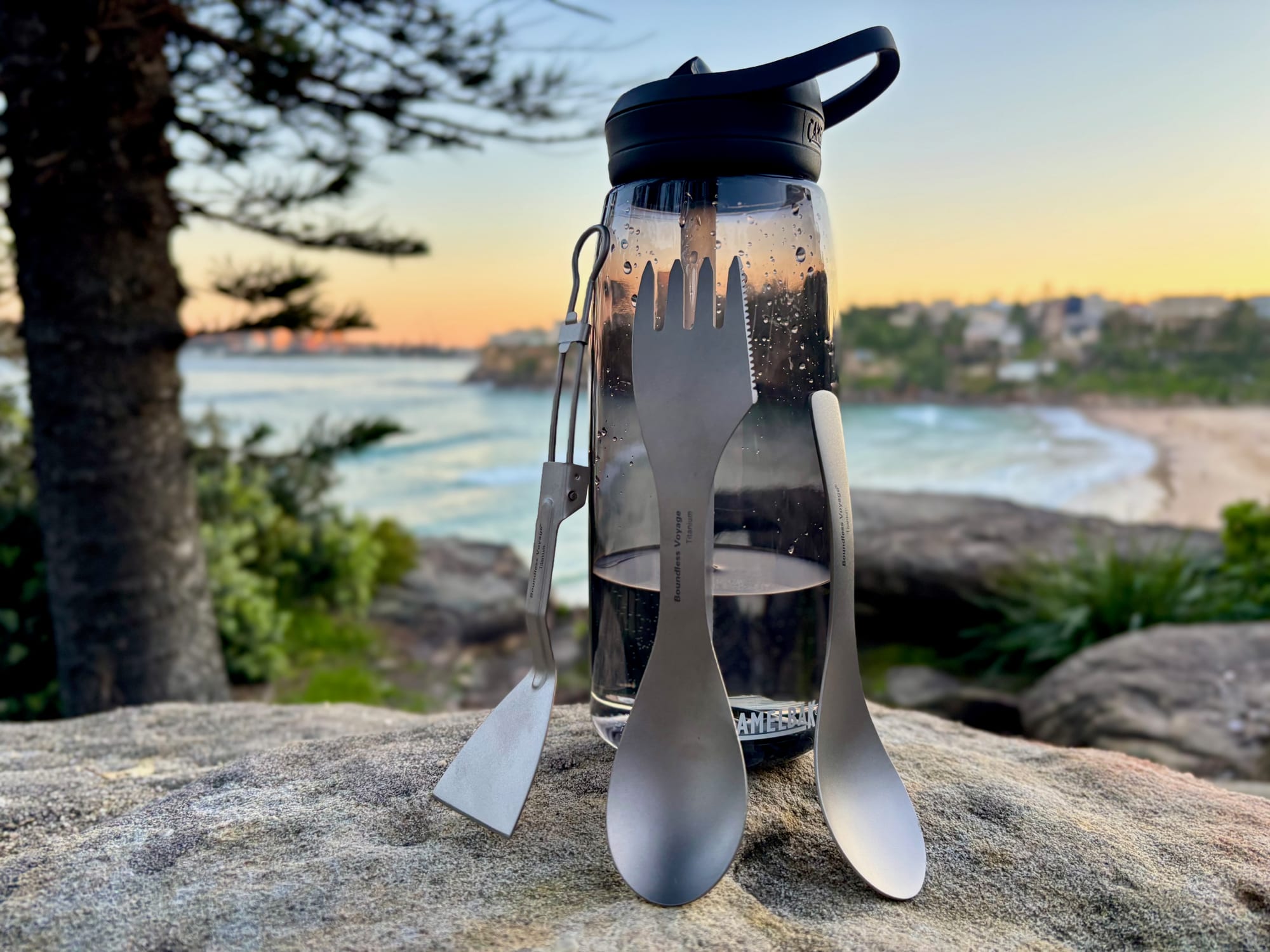 The titanium spoon with a titanium spork and the Boundless Voyage spatula next to a CamelBak Eddy+ water bottle