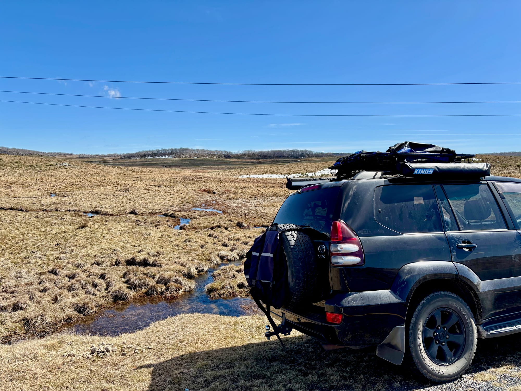 Our 4WD beside the Snowy Mountains Highway on an open high plain, with a creek winding through the grass
