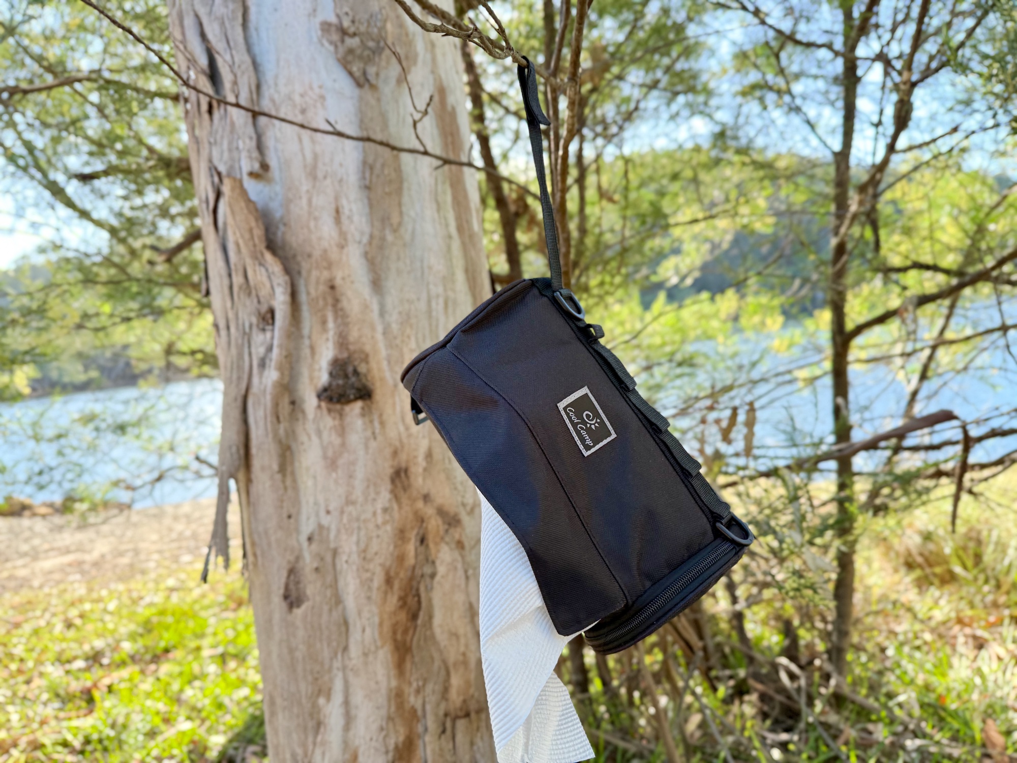 The paper towel holder hanging from a gum tree by a lake, with paper towel coming out