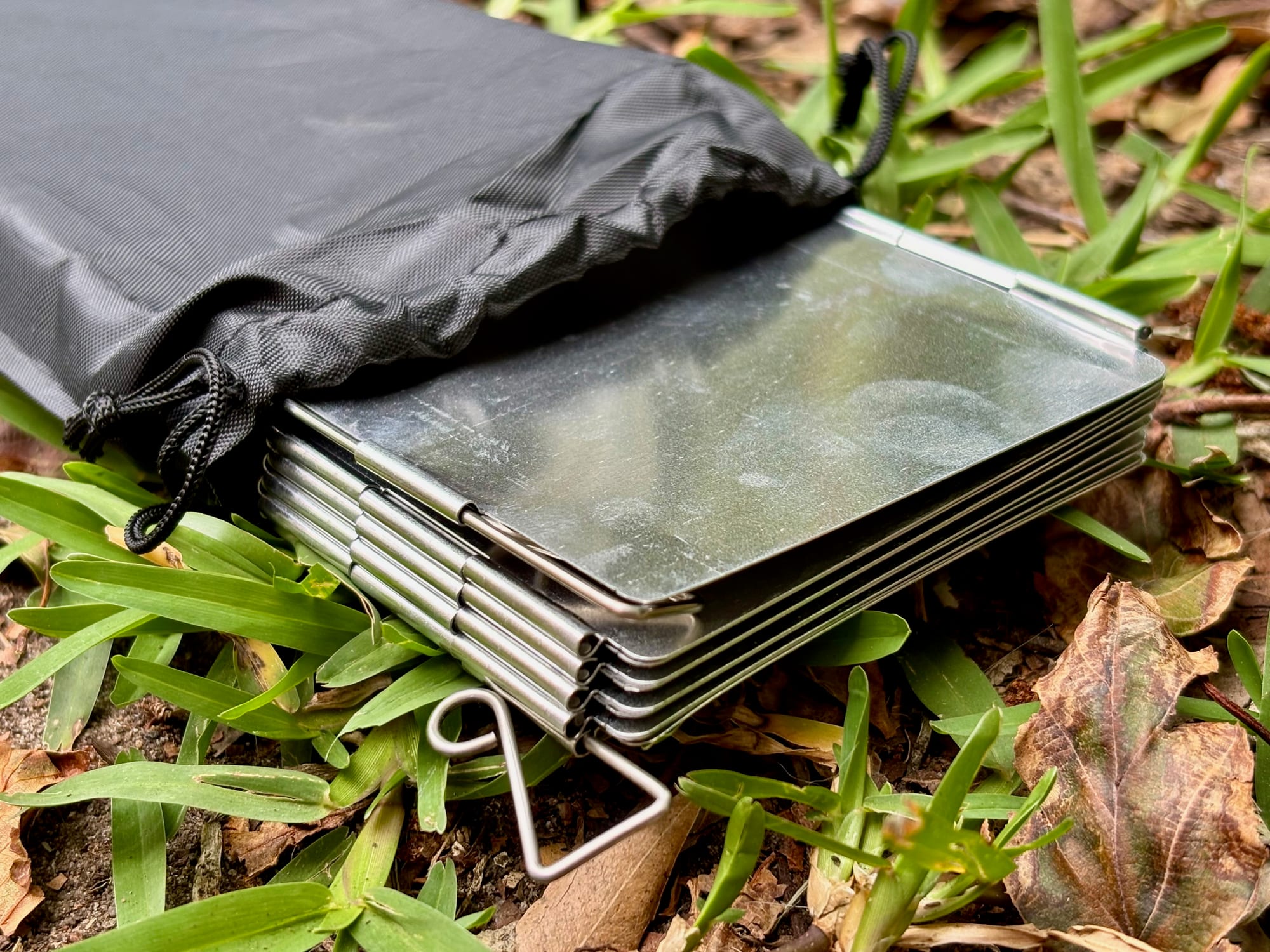 The folding stove windshield folded flat out of its bag, with the wire pegs at the end