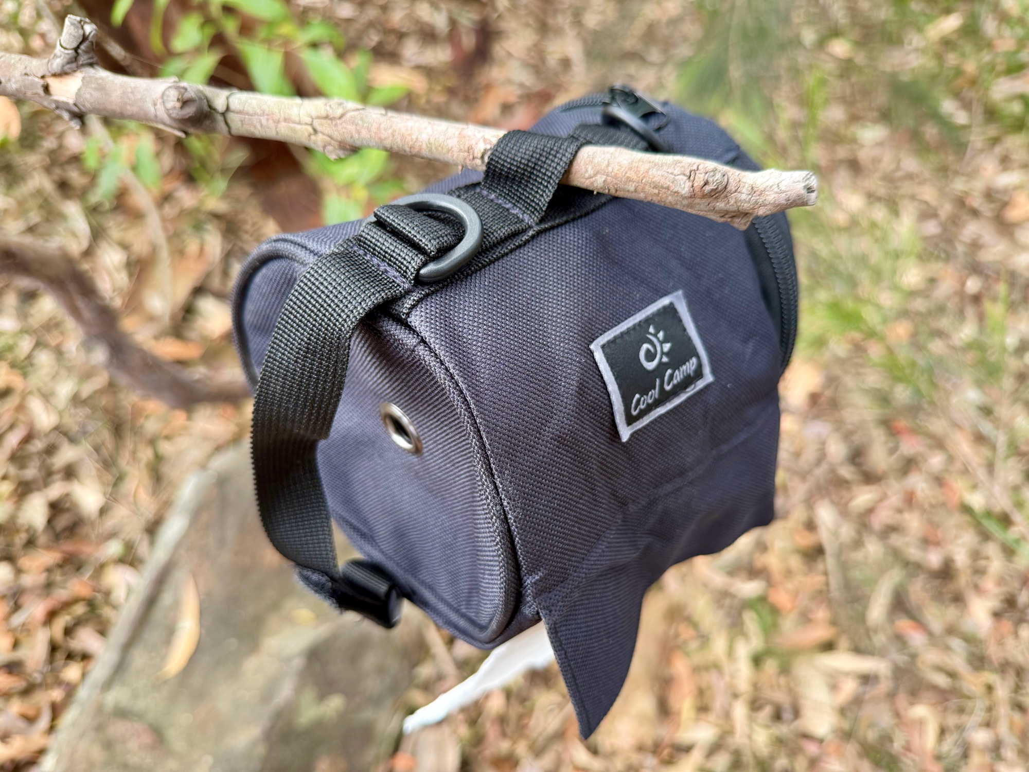 The toilet roll holder hanging from a branch by its strap, with the side flap over the paper