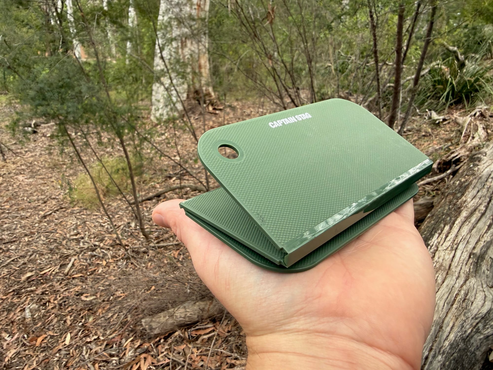 The Captain Stag cutting board folded up in the palm of a hand in the bush