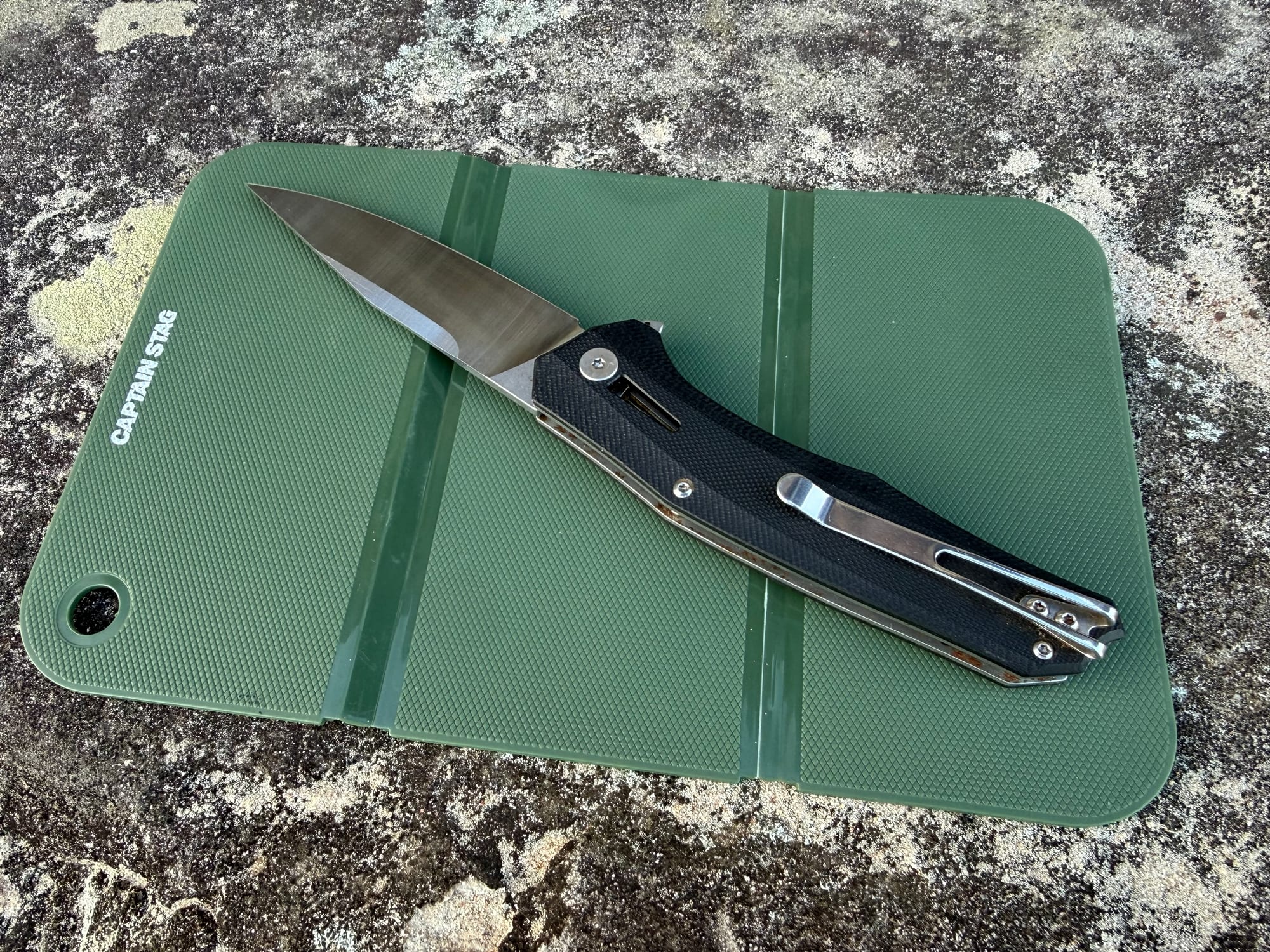 The open Captain Stag cutting board with a folding knife on it, on a sandstone rock