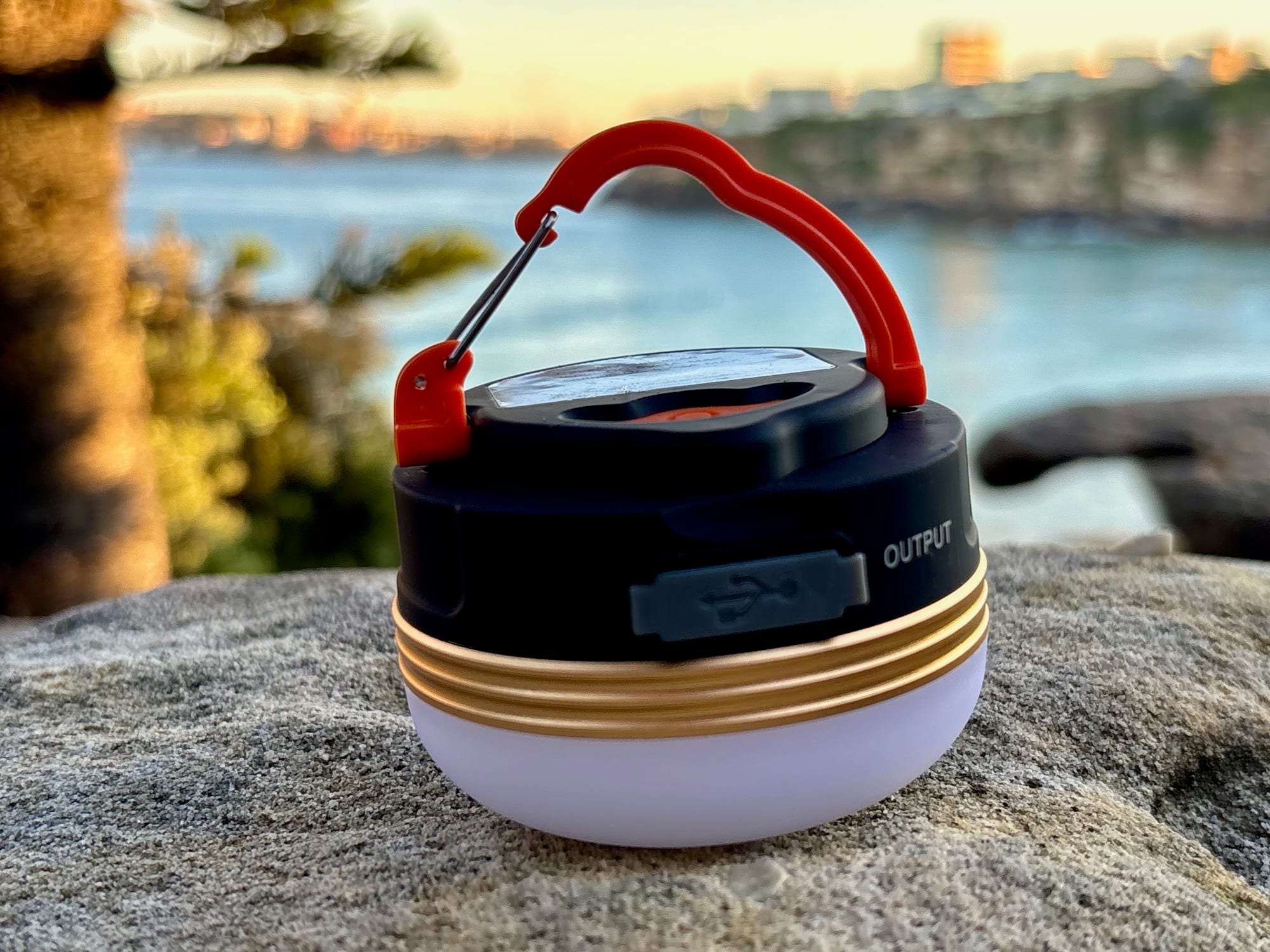The Clearhill camping lantern on a rock above the water, showing the gold band between the black top and the frosted diffuser