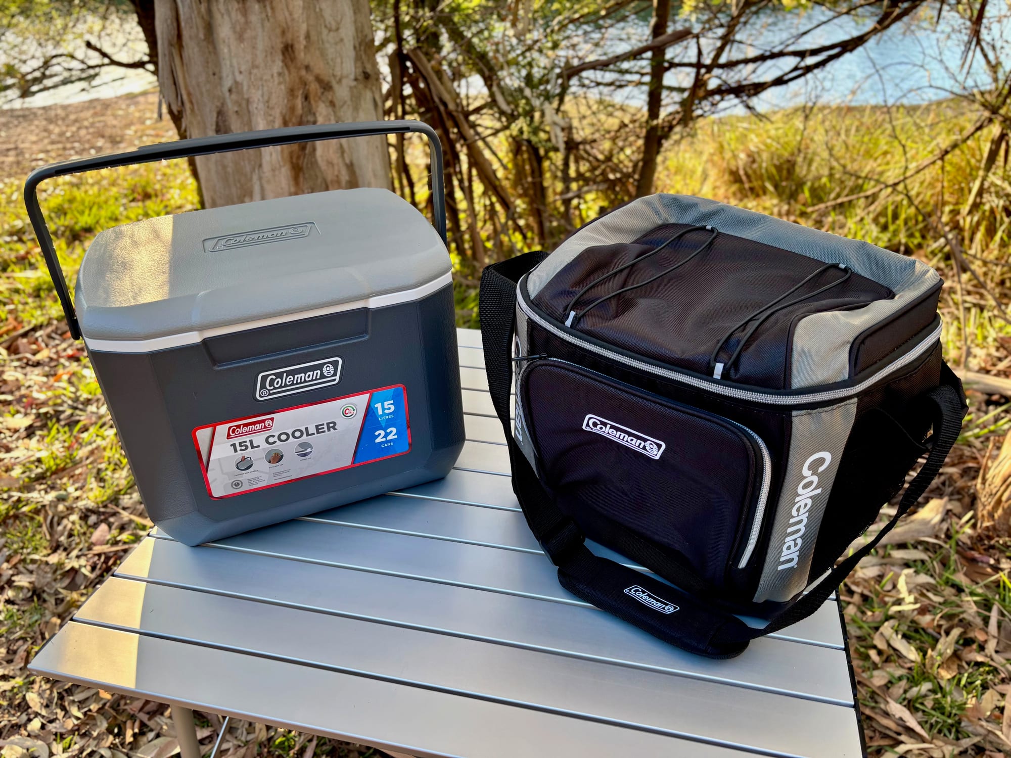 The Coleman 15L hard cooler next to the Coleman 30 Can Soft Cooler on a camp table