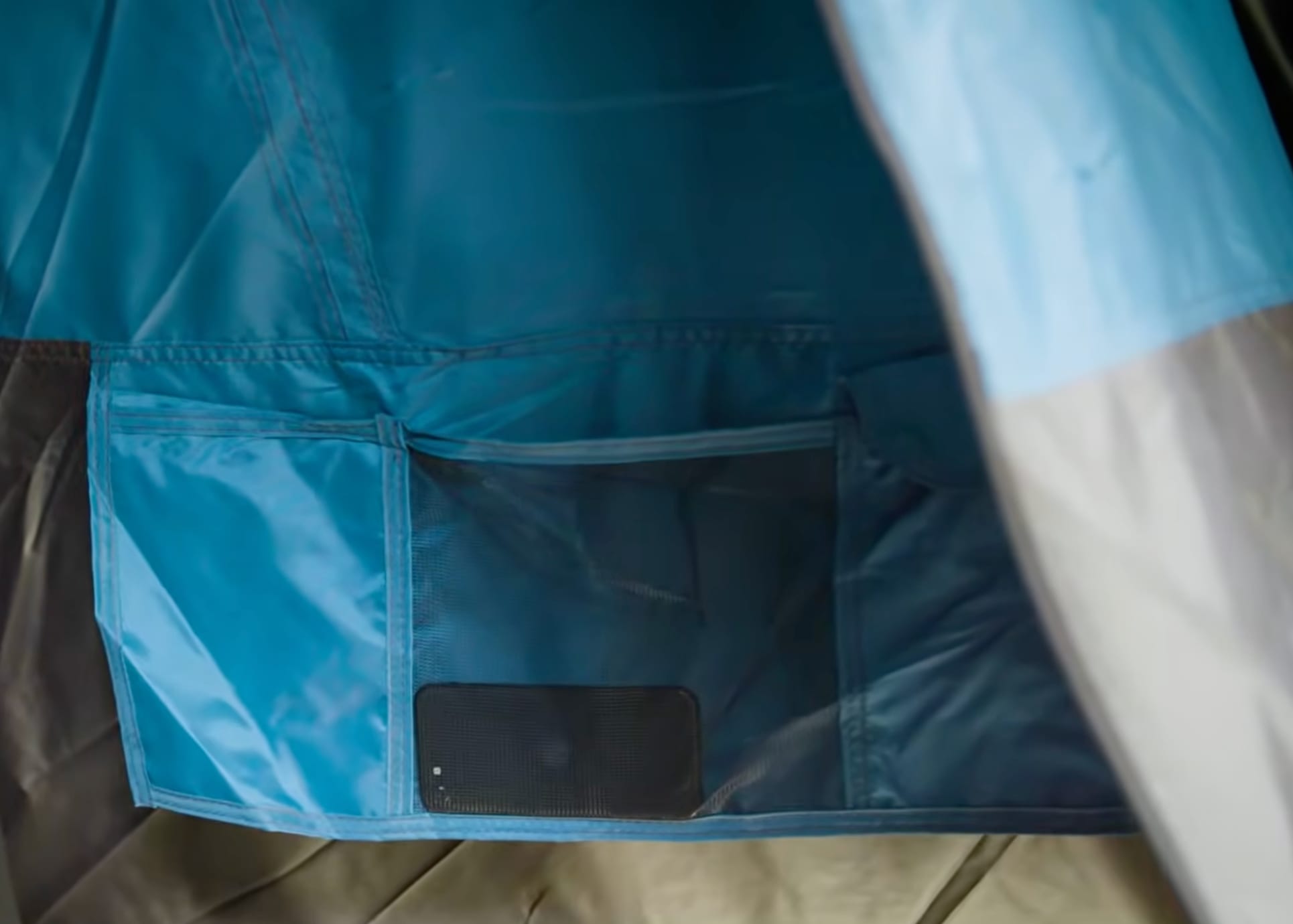 Blue storage pockets on the inside wall of the Coleman tent, with a phone in the mesh pocket