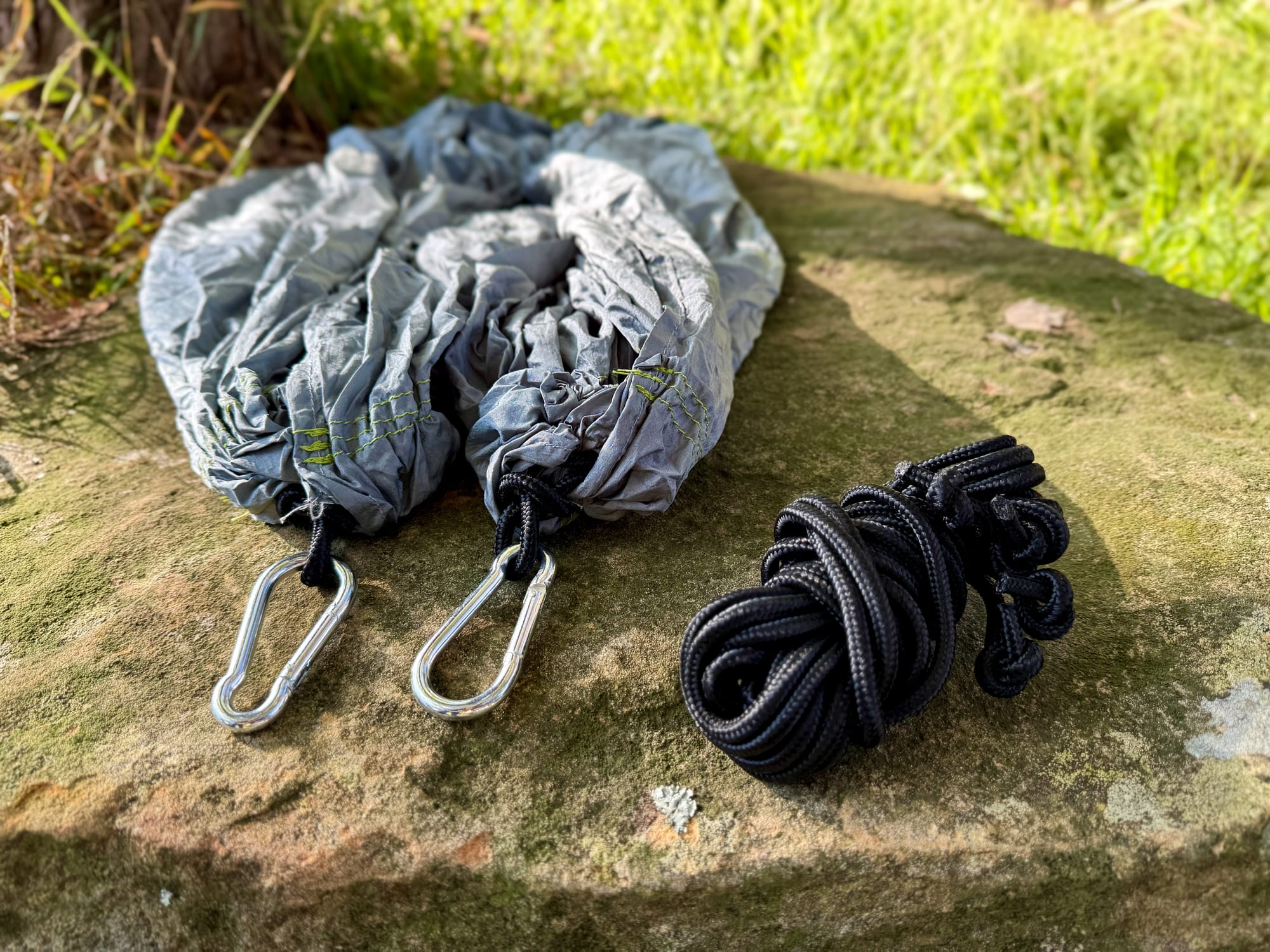 The Coleman hammock, two black ropes and two steel carabiners laid out on a rock