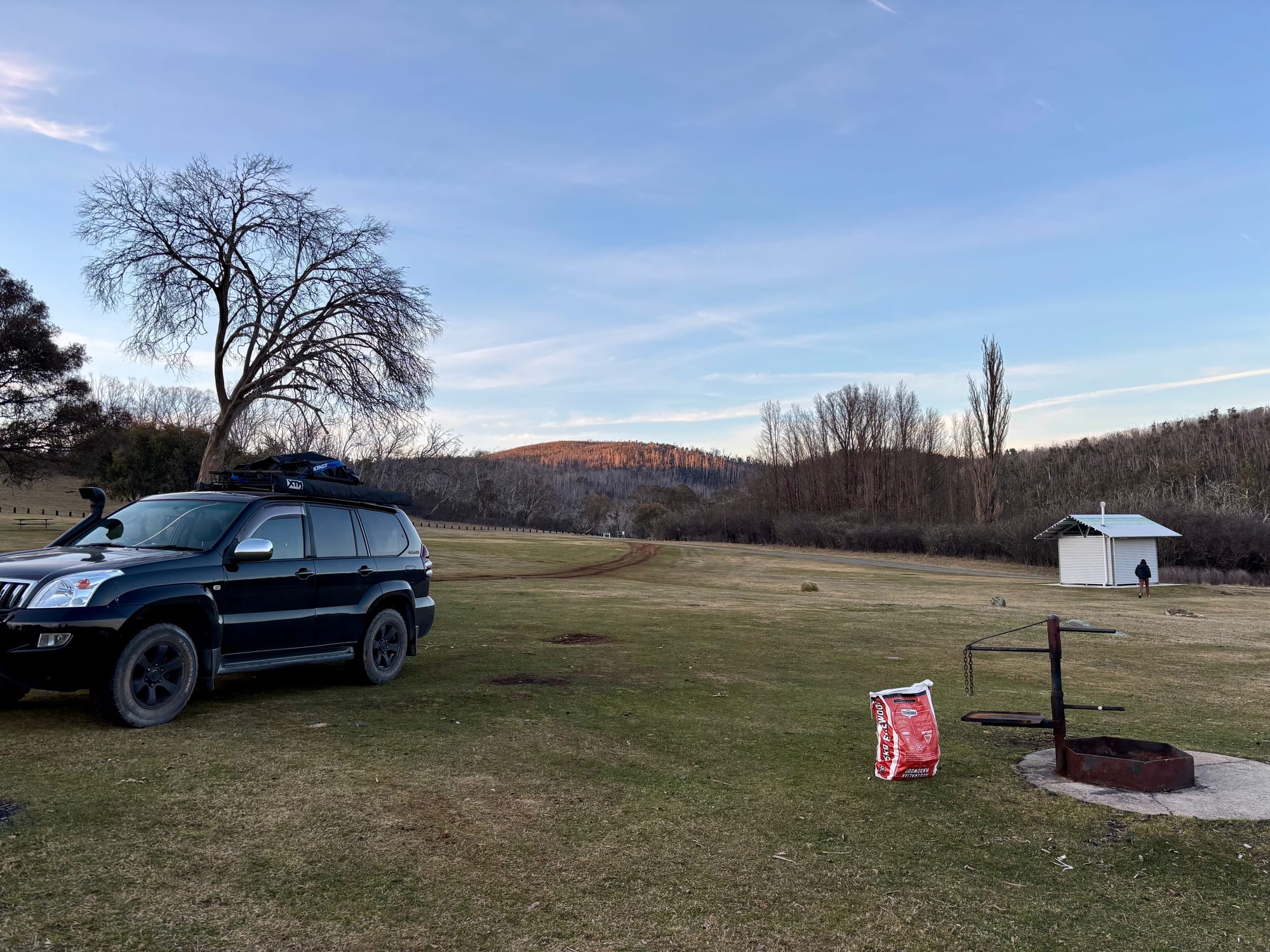 Our 4WD parked next to a fire ring with a bag of firewood at Denison Campground, late in the afternoon