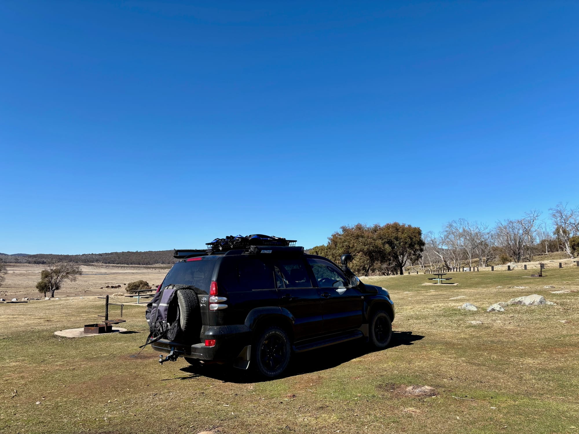 Our 4WD parked next to a fire ring on the open grass at Denison Campground, with the plain and hills behind
