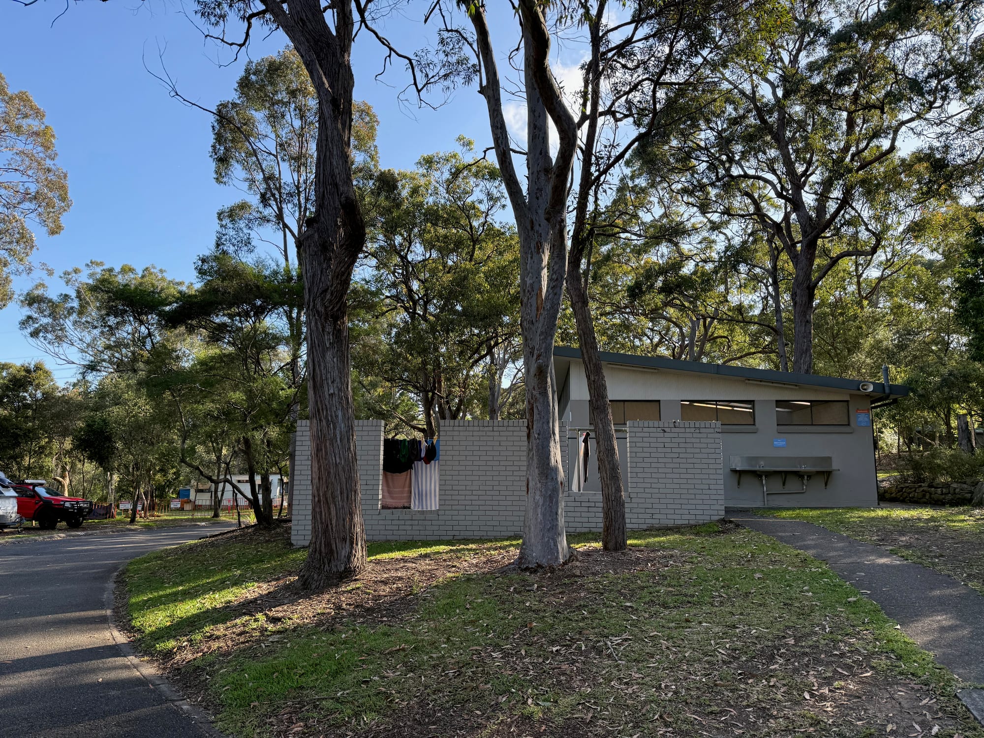 A toilet block on the grass under the gum trees at Discovery Parks Lane Cove, with caravans behind