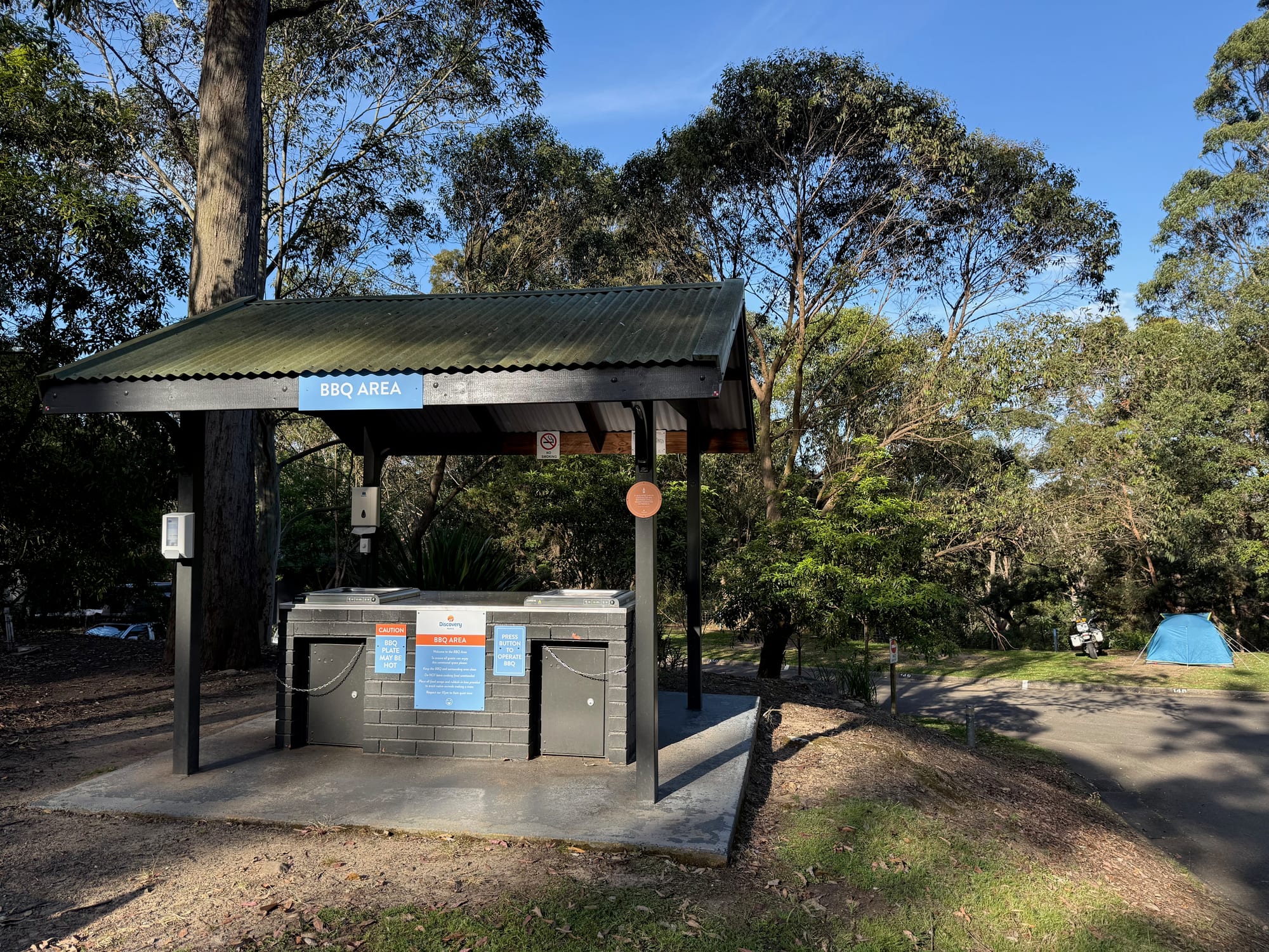 A covered barbecue area with two barbecues next to the sites at Discovery Parks Lane Cove
