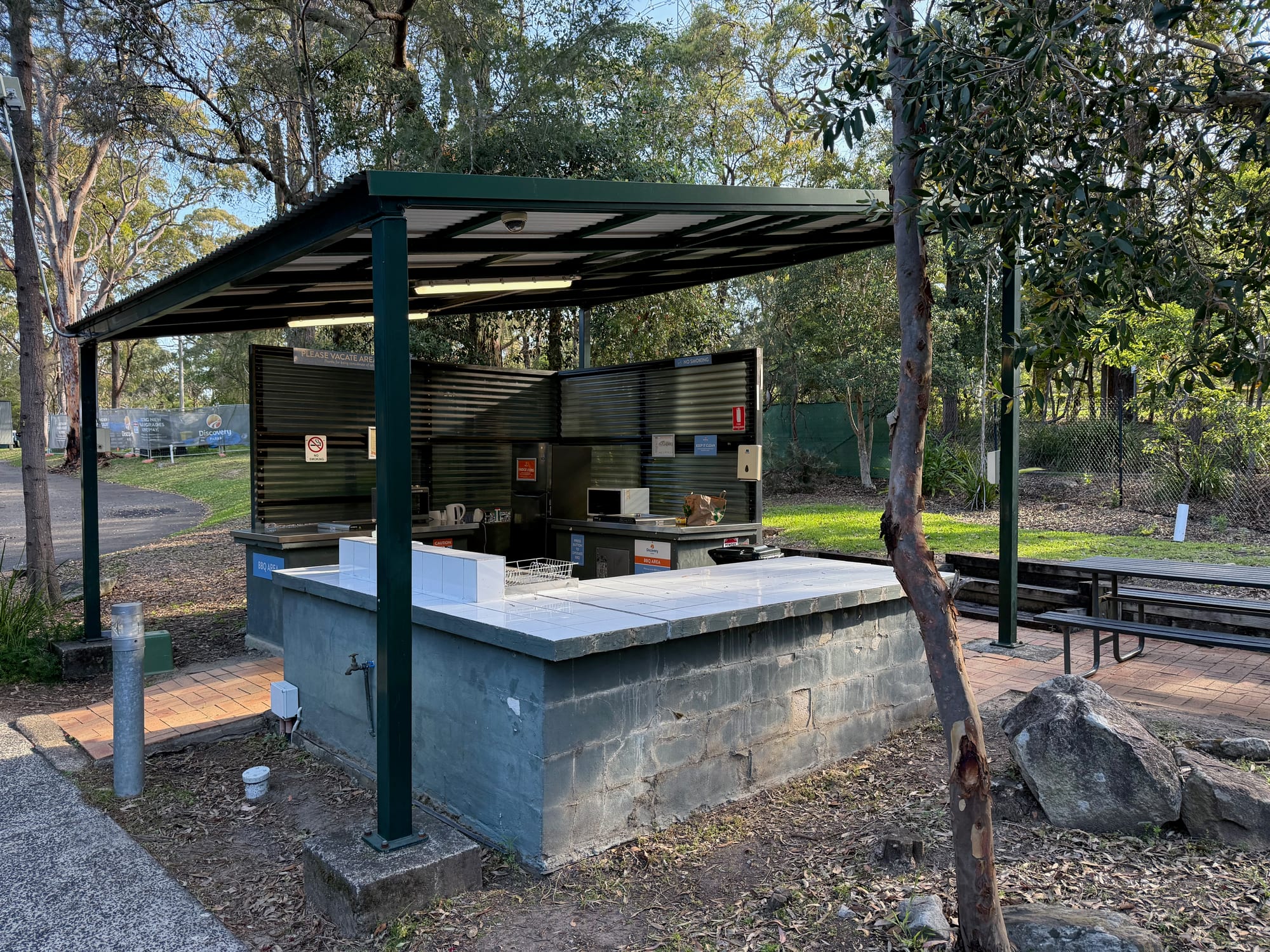 A covered camp kitchen with a sink bench and picnic tables at Discovery Parks Lane Cove