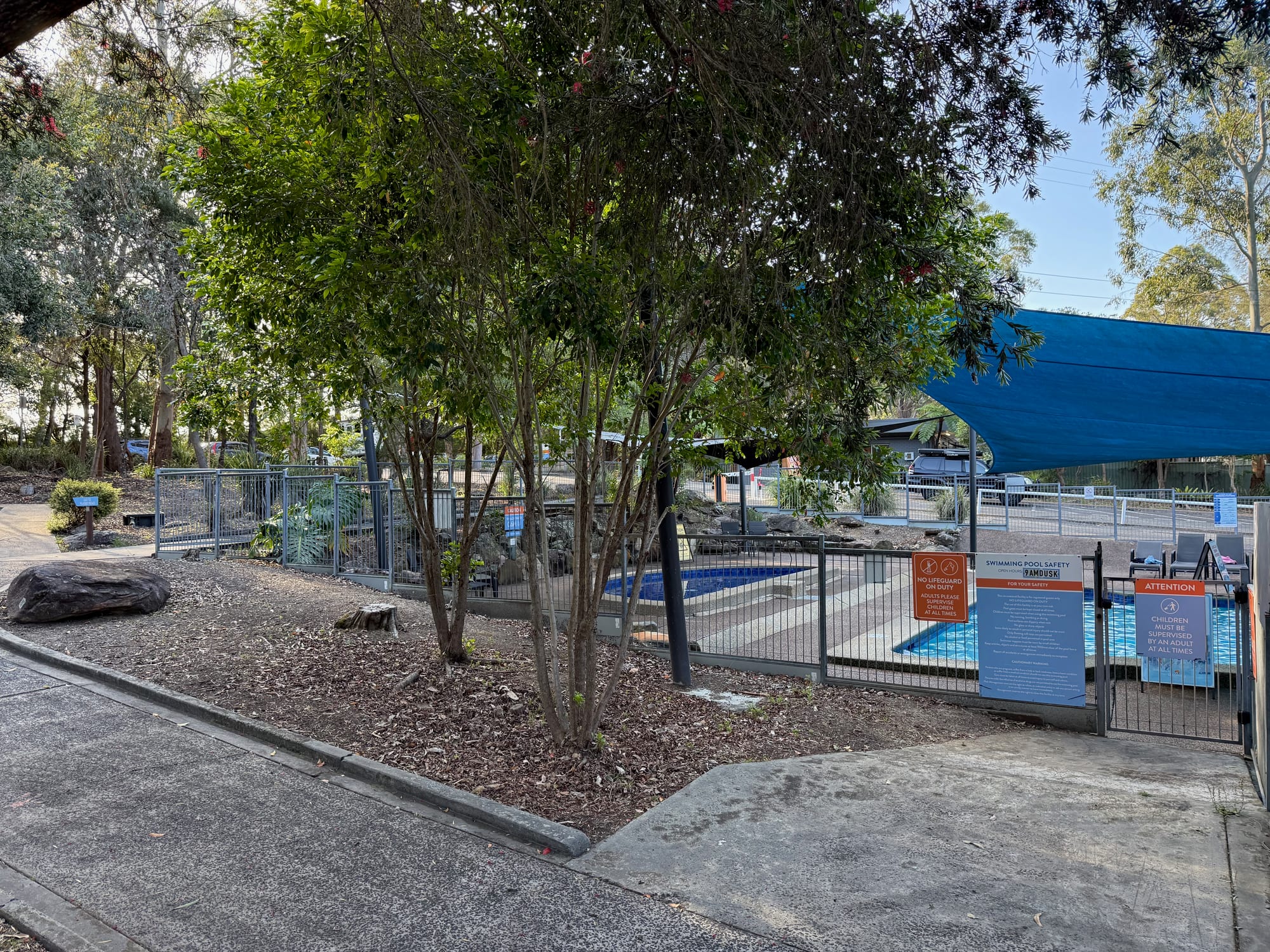 The fenced outdoor pool under a shade sail near the reception of Discovery Parks Lane Cove