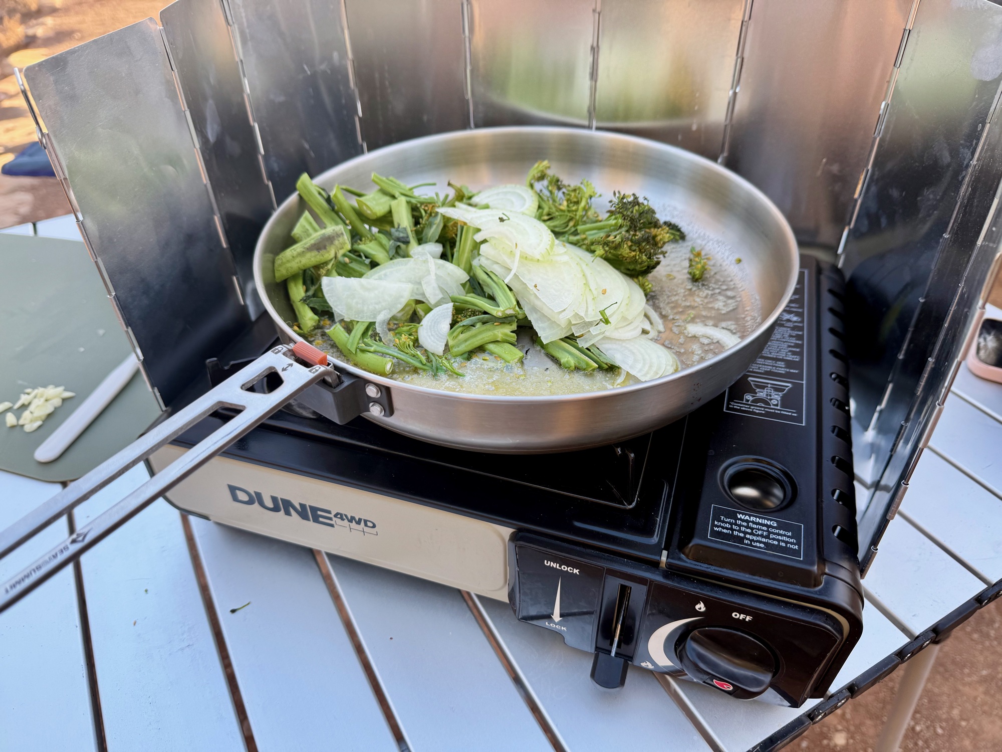 Cooking greens and onion in a frying pan on the Dune 4WD stove behind a windshield