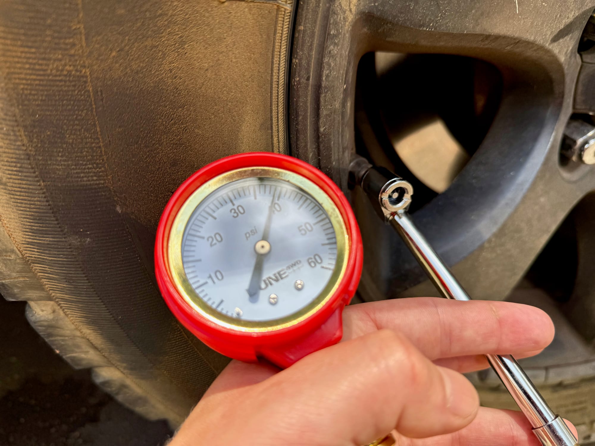 The chrome chuck of the Dune 4WD gauge on a tyre valve, with the dial held in the hand