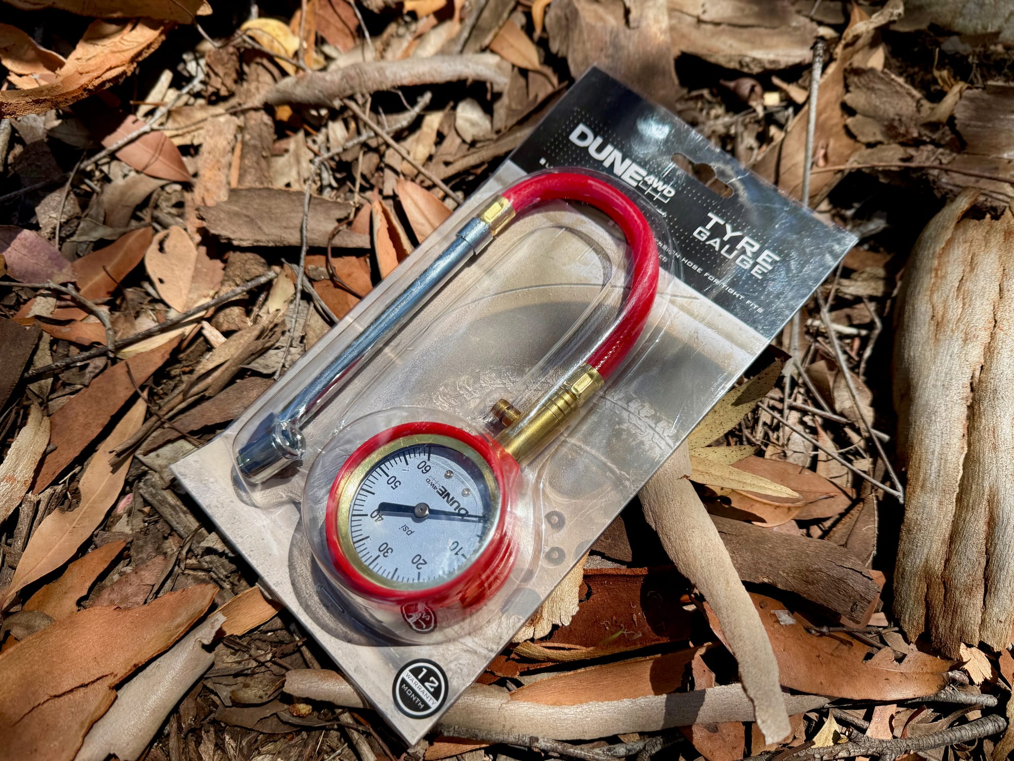 The Dune 4WD Tyre Gauge in its packaging, lying on dry leaves